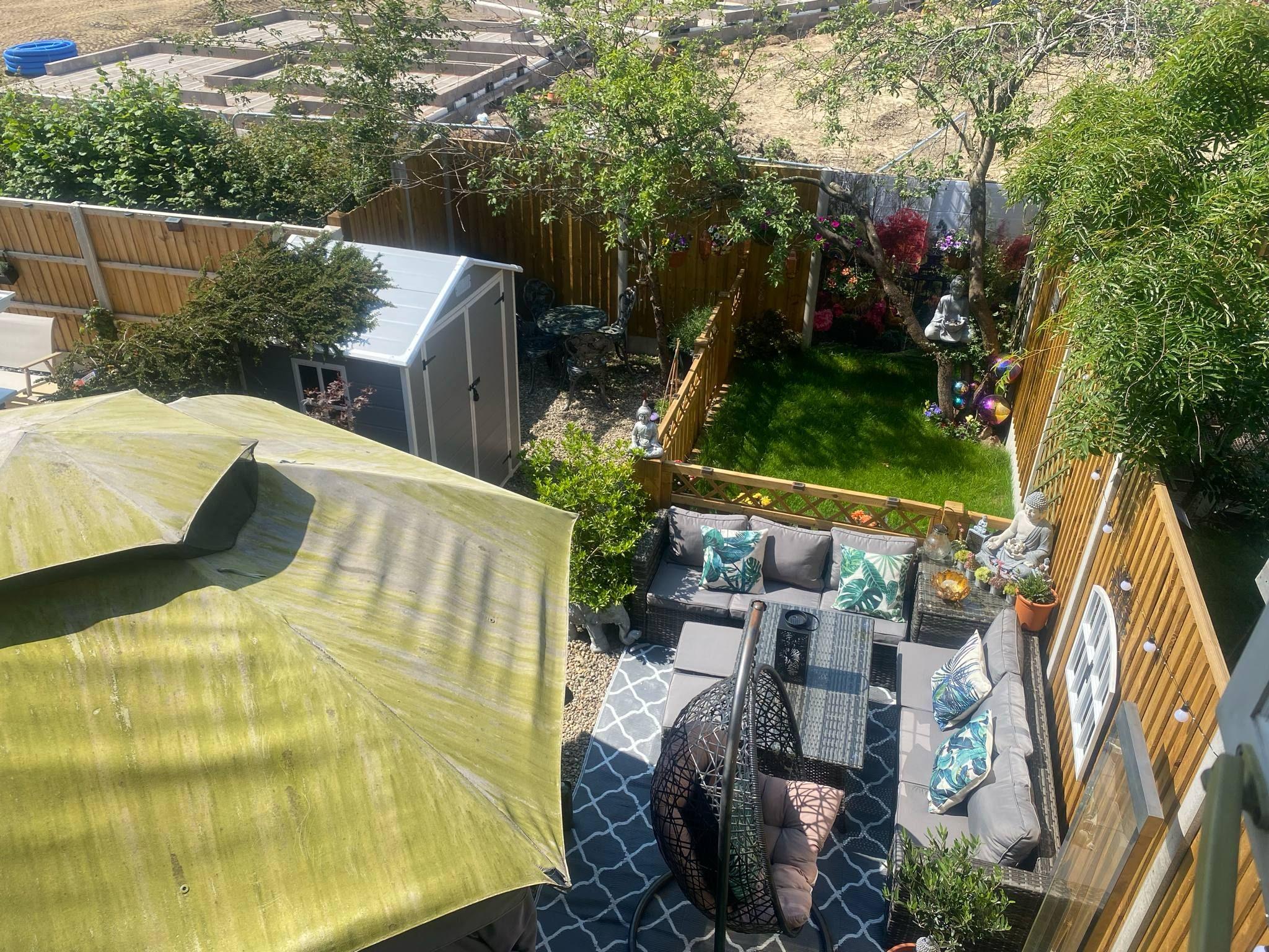 A shot from an upstairs window showing the length of the garden with development in the field behind. The garden has a gazebo and grey wicker-style furniture, with a fenced-off lawn area at the back and a grey plastic shed to one side.
