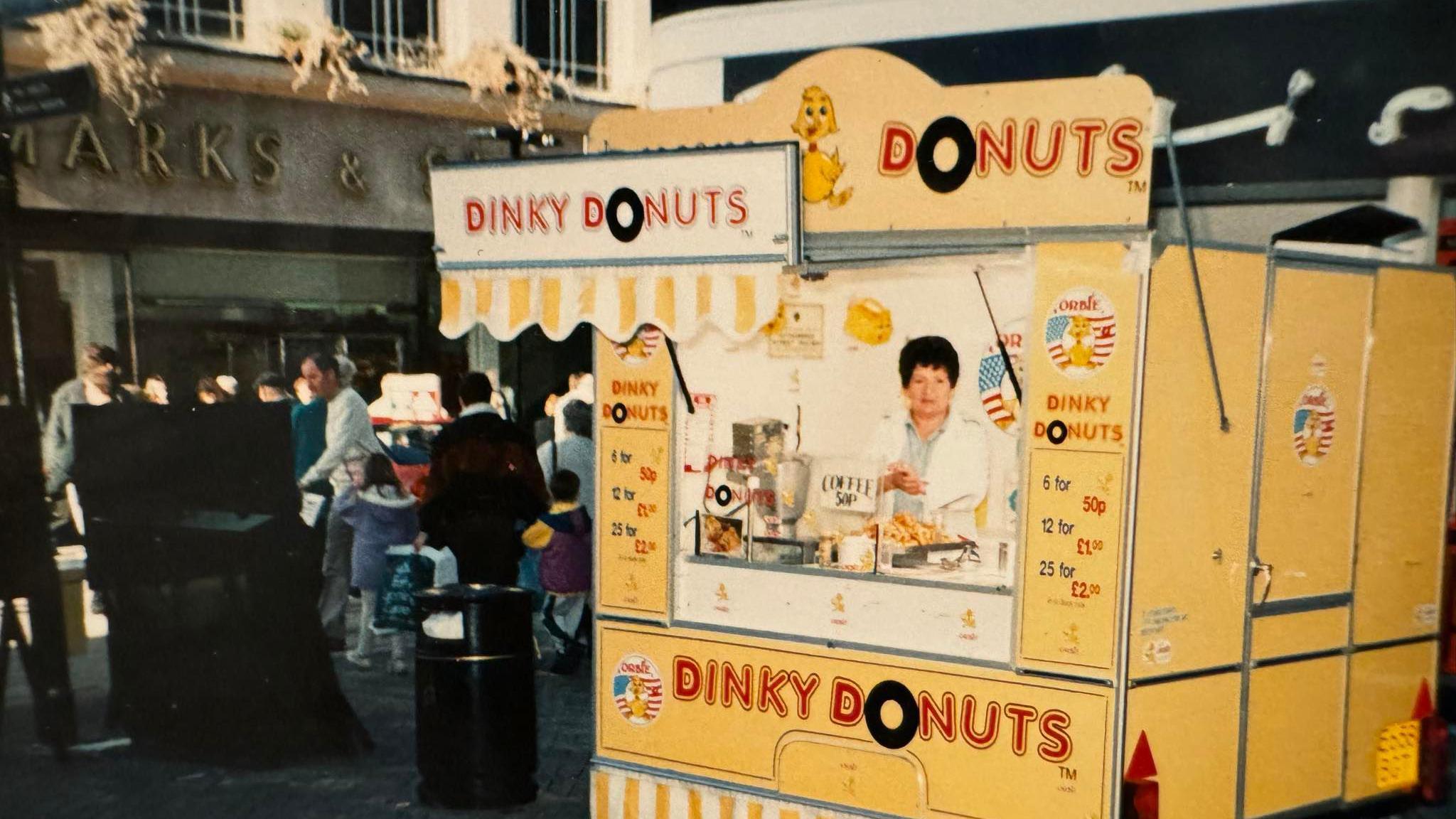 Lina working from her bright yellow doughnut stall in Bedford several years ago, with shoppers walking past the M&S.