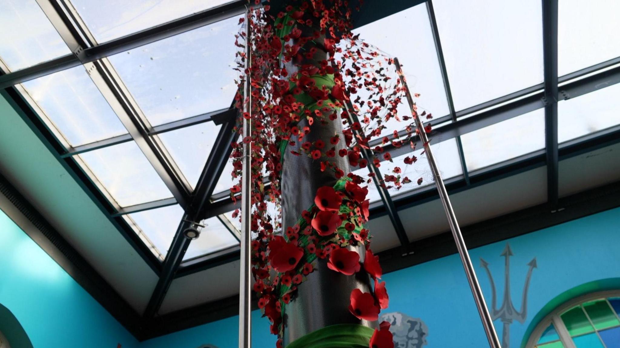 The picture shows a black pole running down the middle. It's adorned with red poppies of different sizes. Above is is a glass roof.