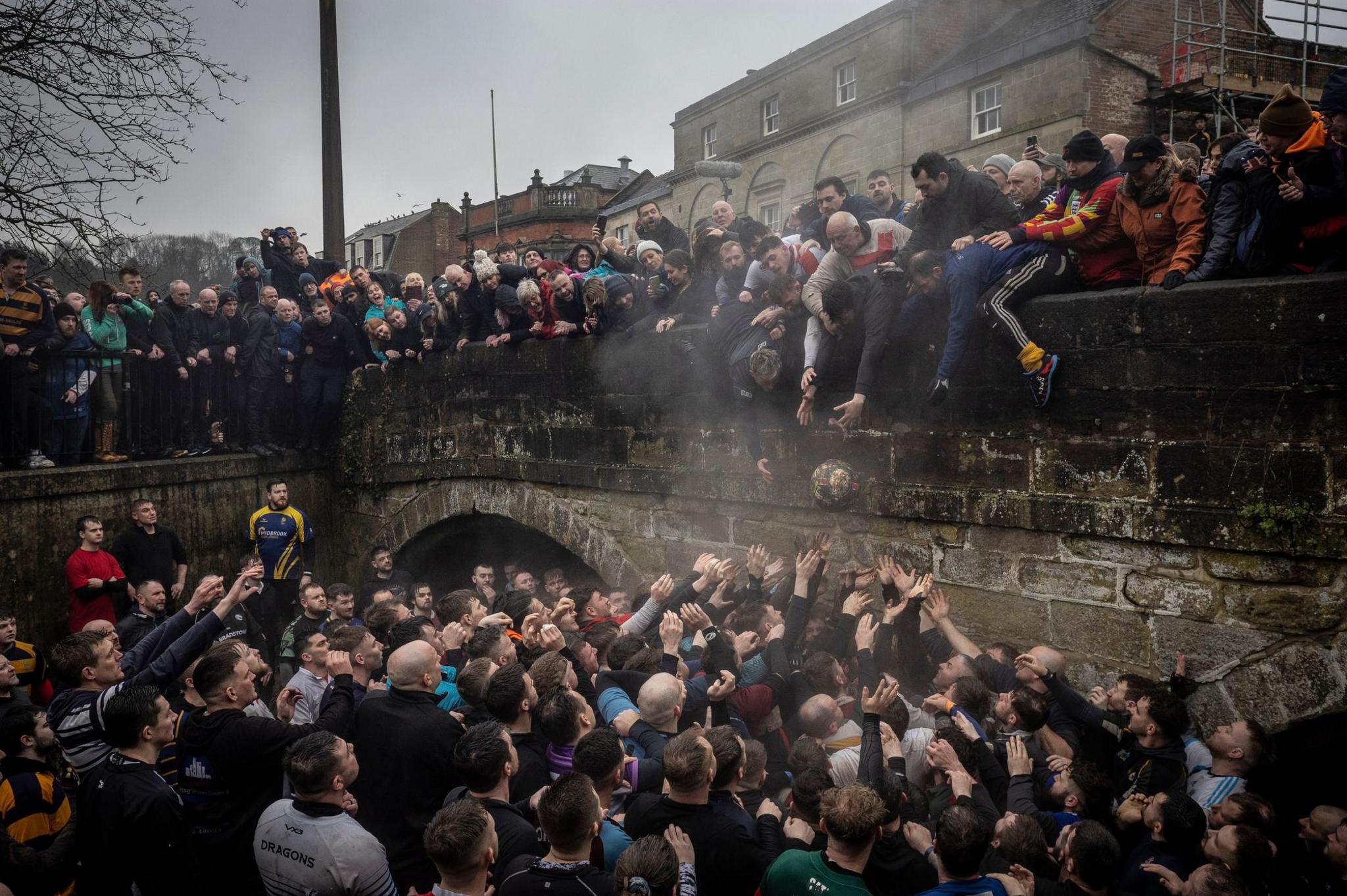 Crowds of people chase the ball beside a bridge