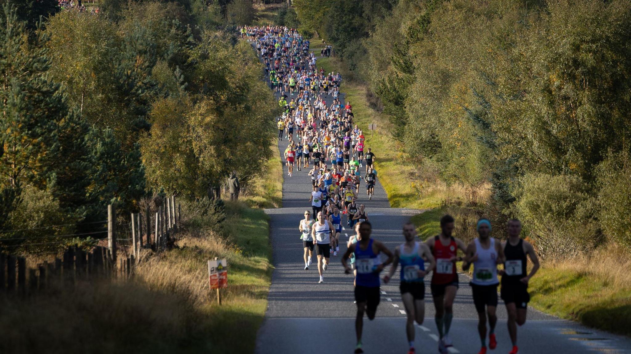 hundreds of people running on a long stretch of road through woodland