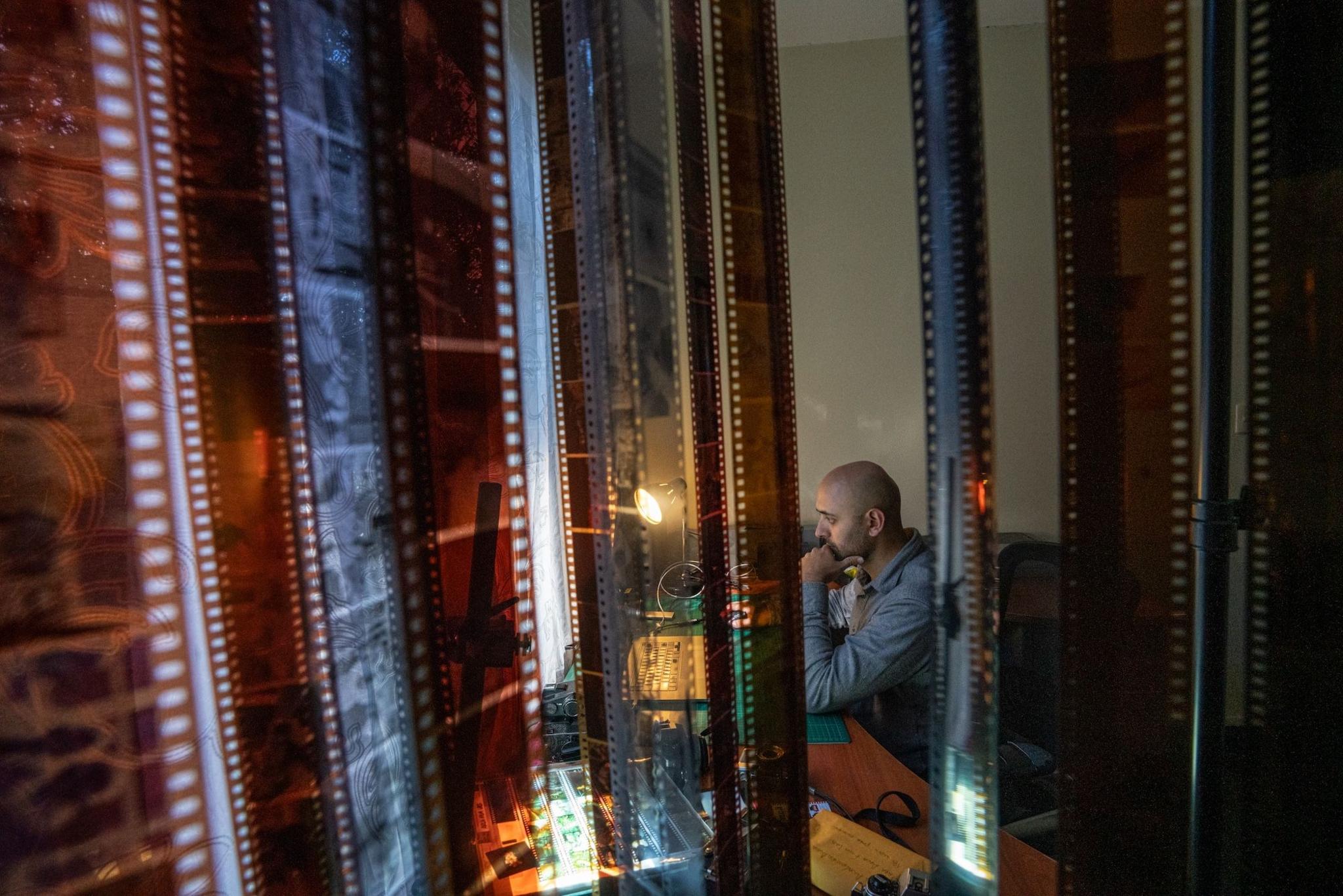 Fabriccio Díaz is working on his computer in room of their apartment that has been converted into an office. In the foreground, rolls of film are hanging to dry. 