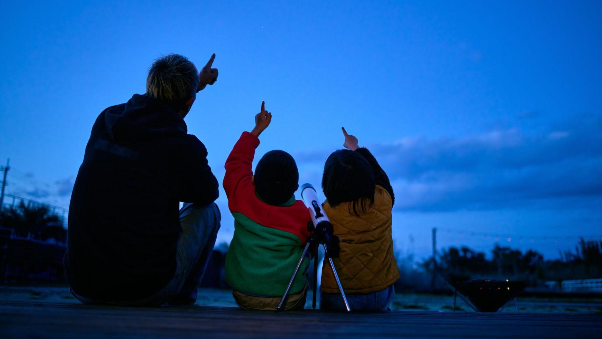 Silhouette of father and son pointing to sky in search of stars