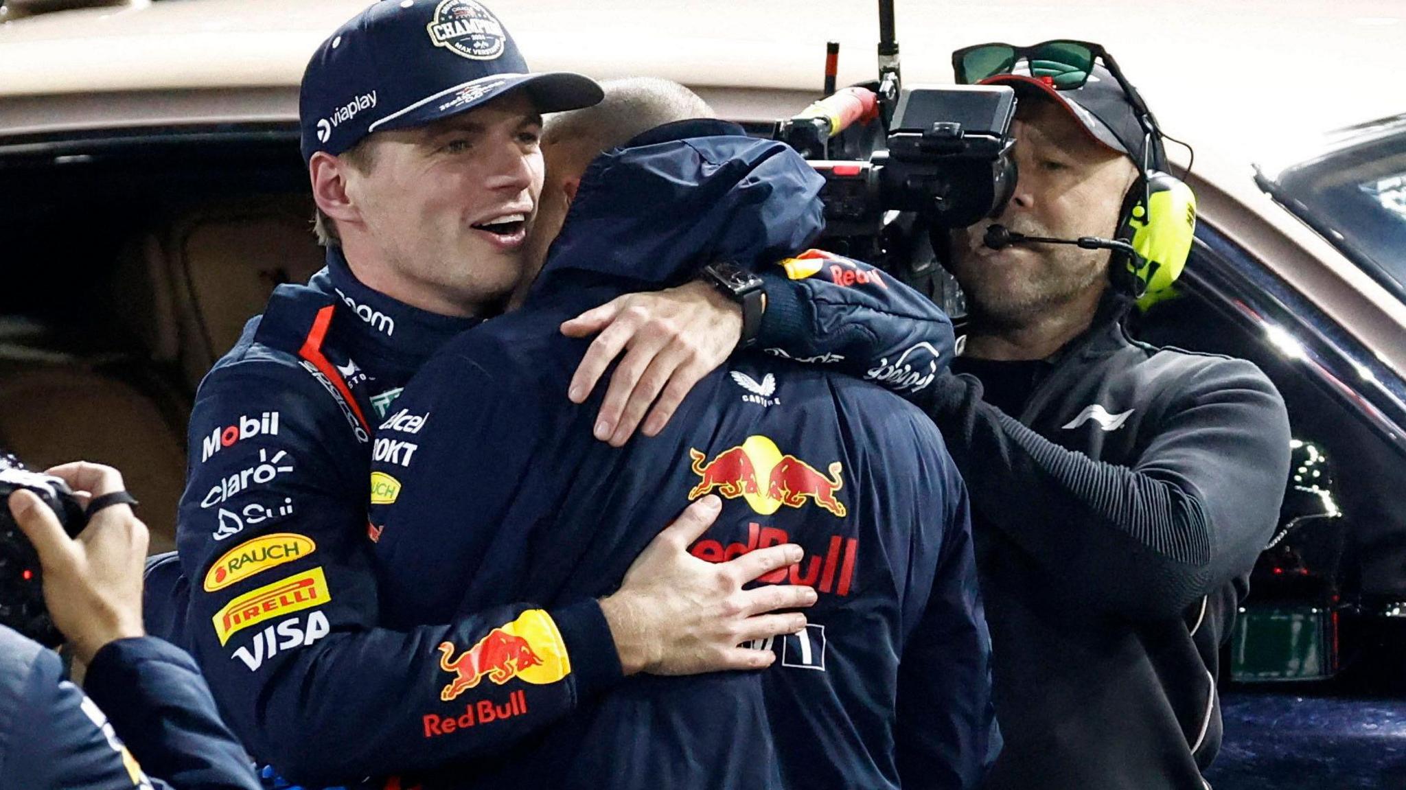 Max Verstappen embraces a Red Bull team member after winning the F1 world title, with a TV cameraman in the background