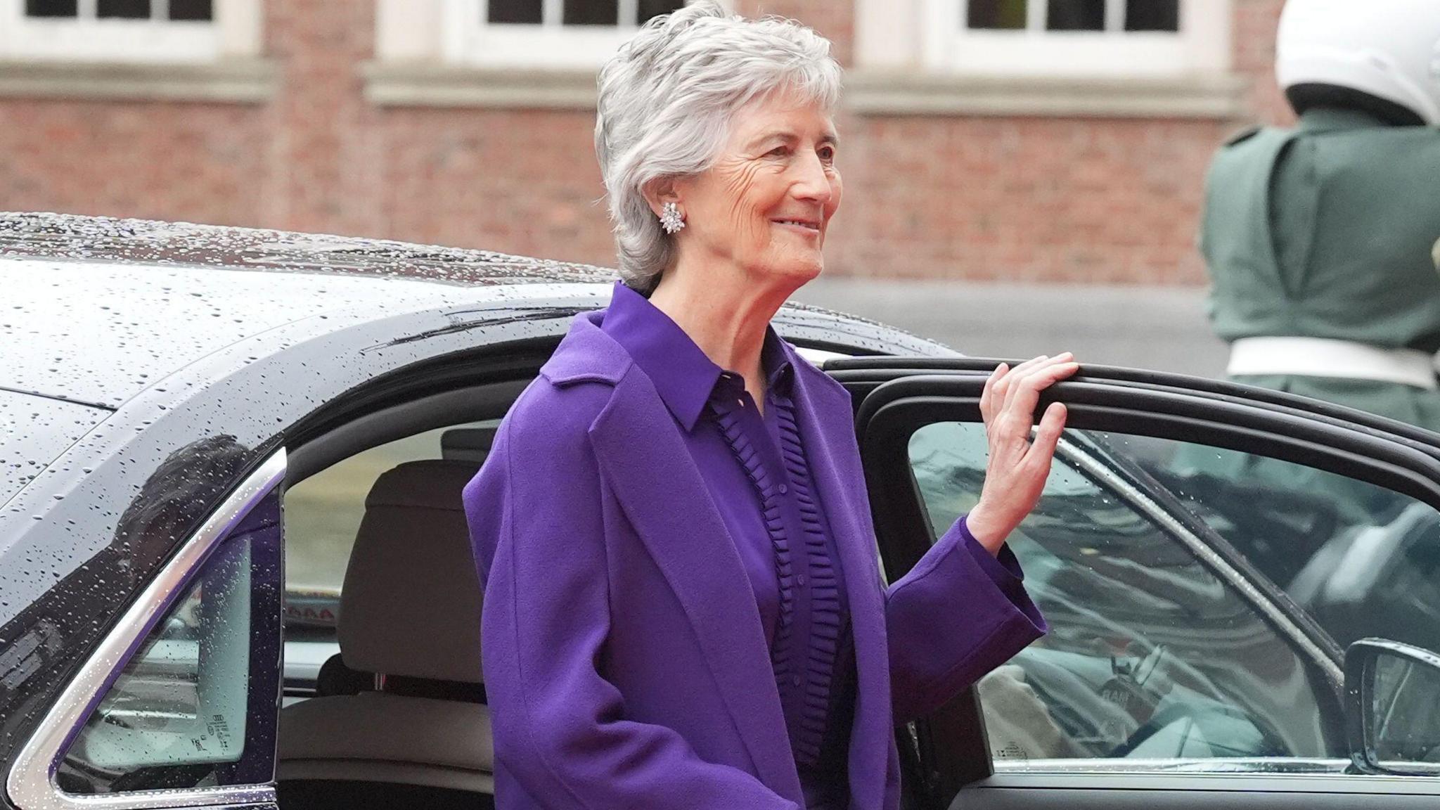 Catherine Connolly stepping out of a black car, she is wearing a purple top and coat, she has grey hair.