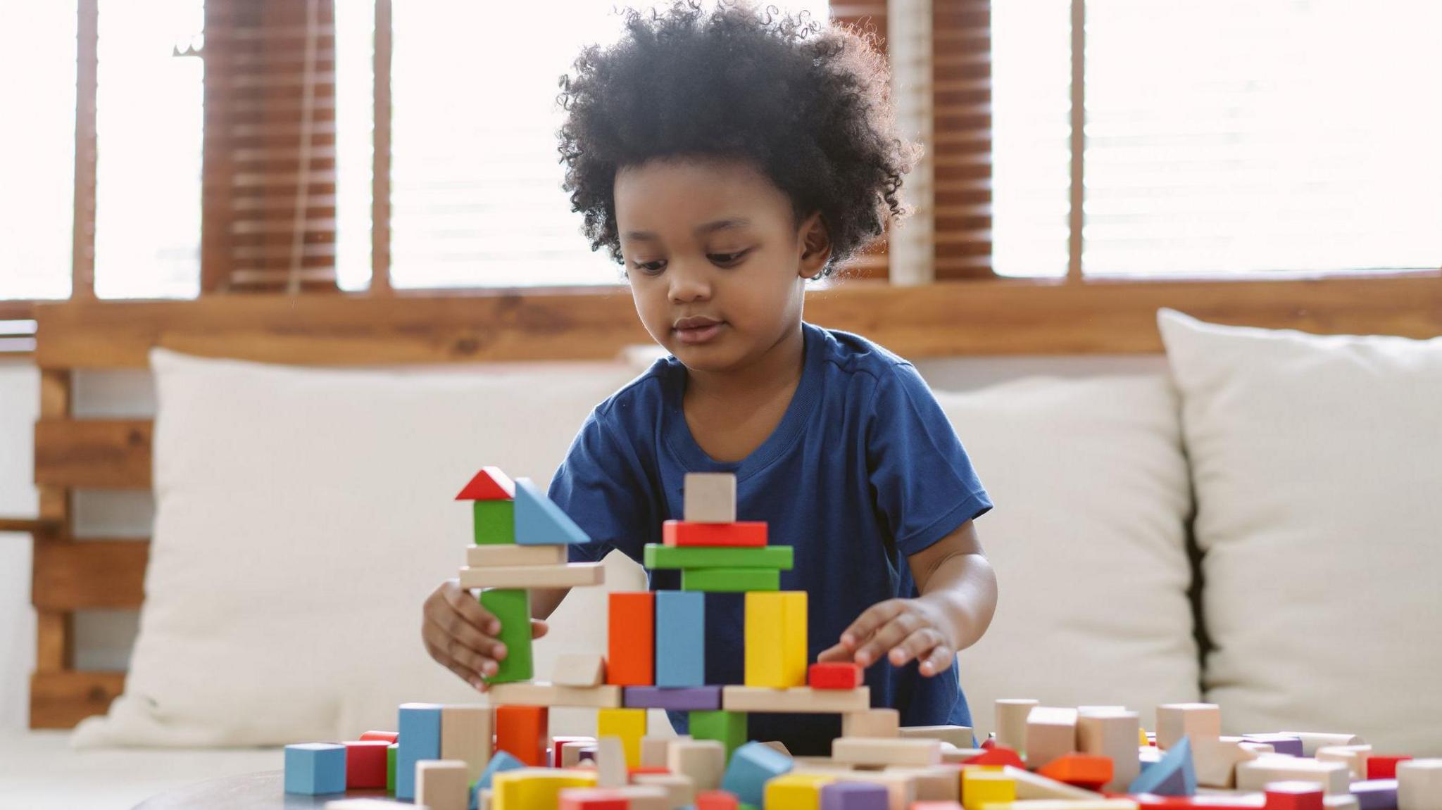 Child playing with wooden coloured bricks on a table in front of a sofa