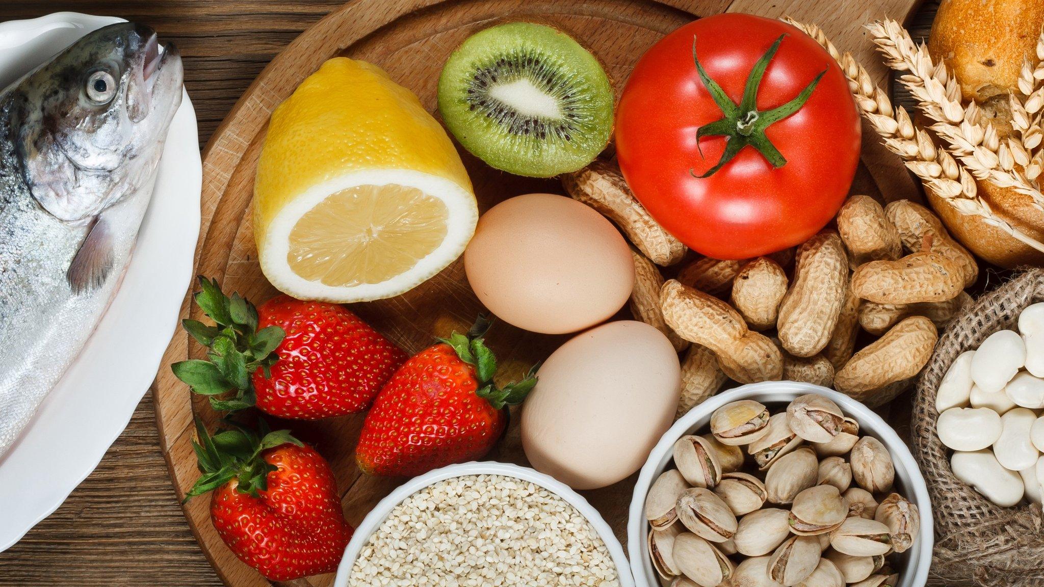 Food allergy concept. Almonds, milk, pistachios, tomato, lemon, kiwi, trout, strawberry, bread, sesame seeds, eggs, peanuts and bean on wooden table