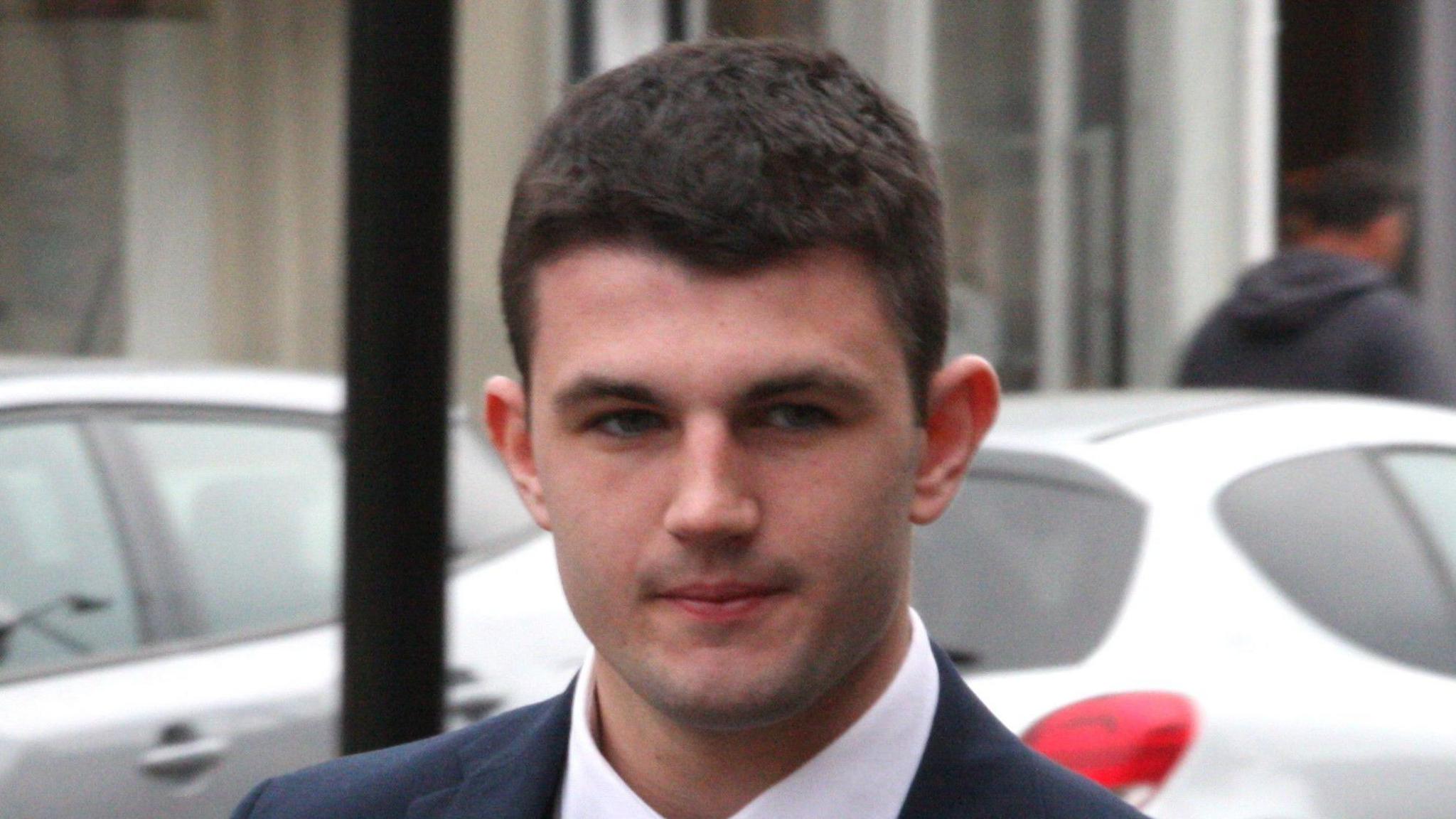 A young man with dark hair wearing a suit is pictured outside