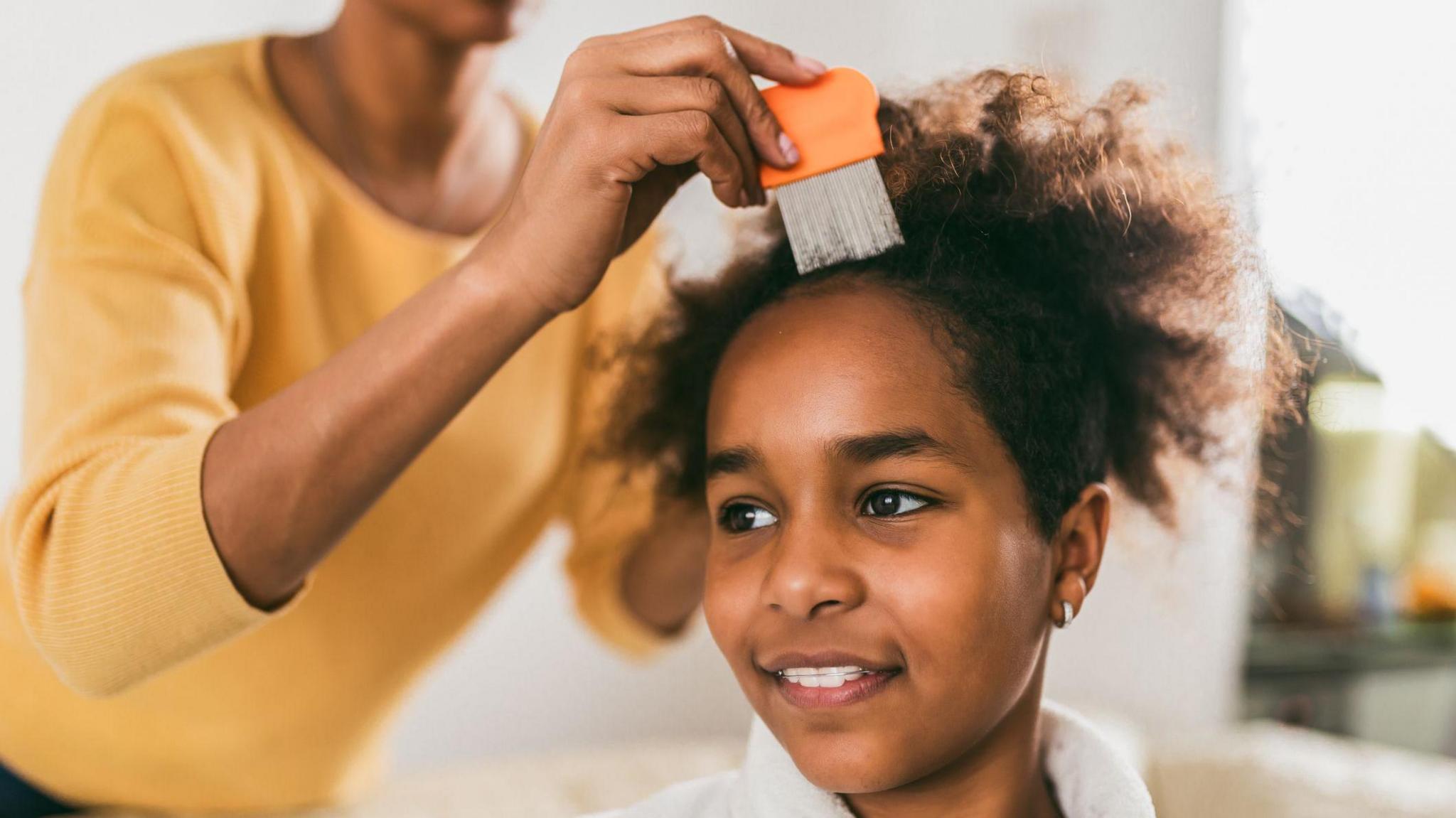 Mother using fine-tooth comb on child's hair. 