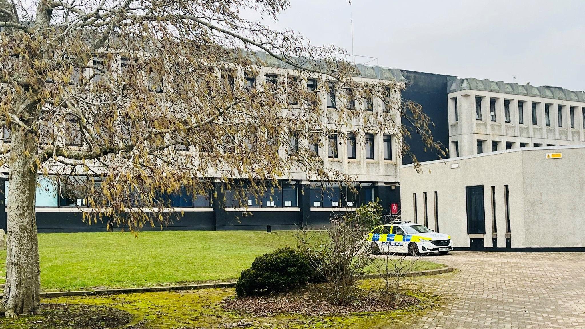 Police car outside a school building, with a tree in the foreground