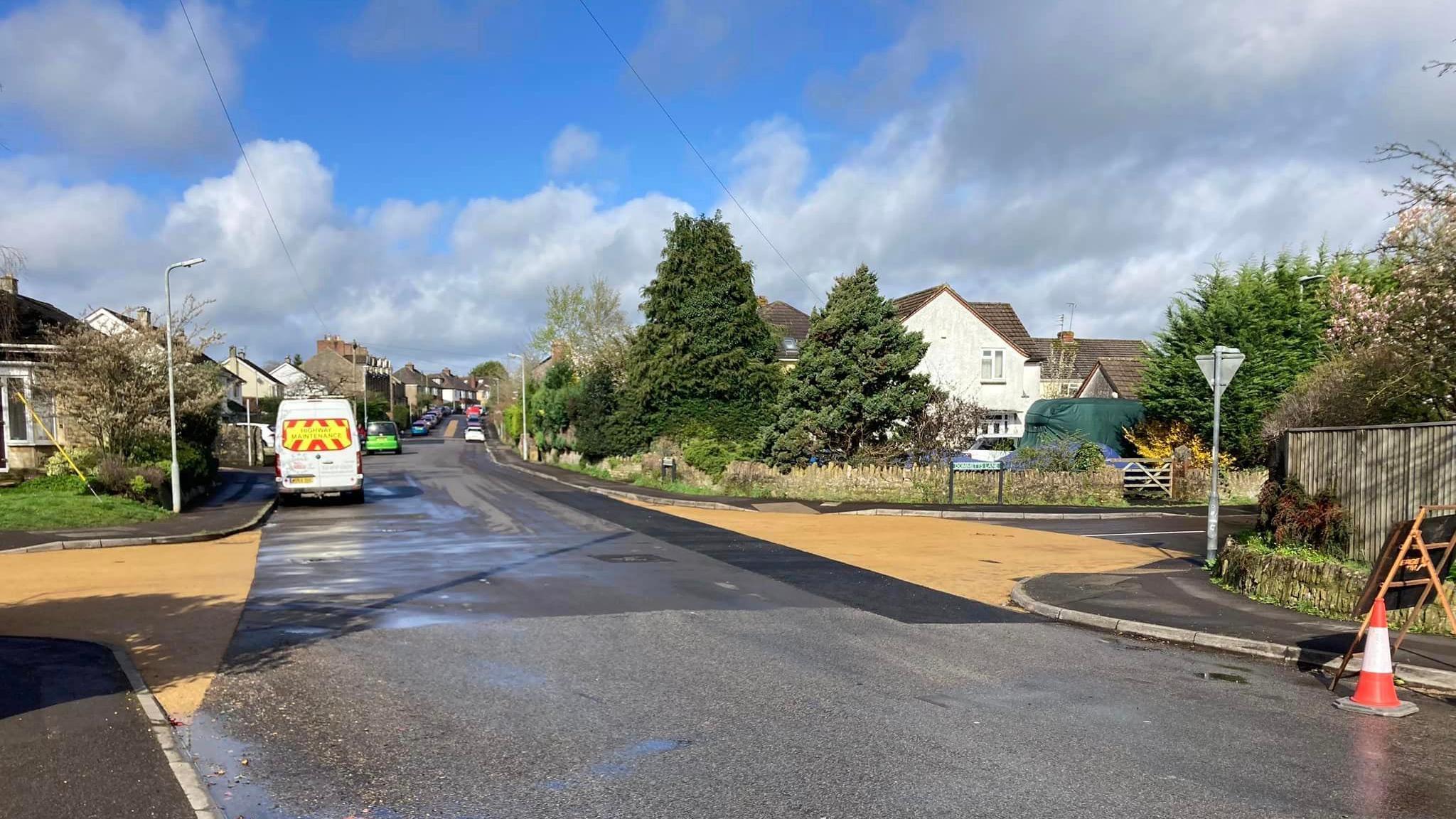 A crossroads on a residential street. The two roads going to the left and right of the image are paved in a lighter colour, indicating drivers should slow down.