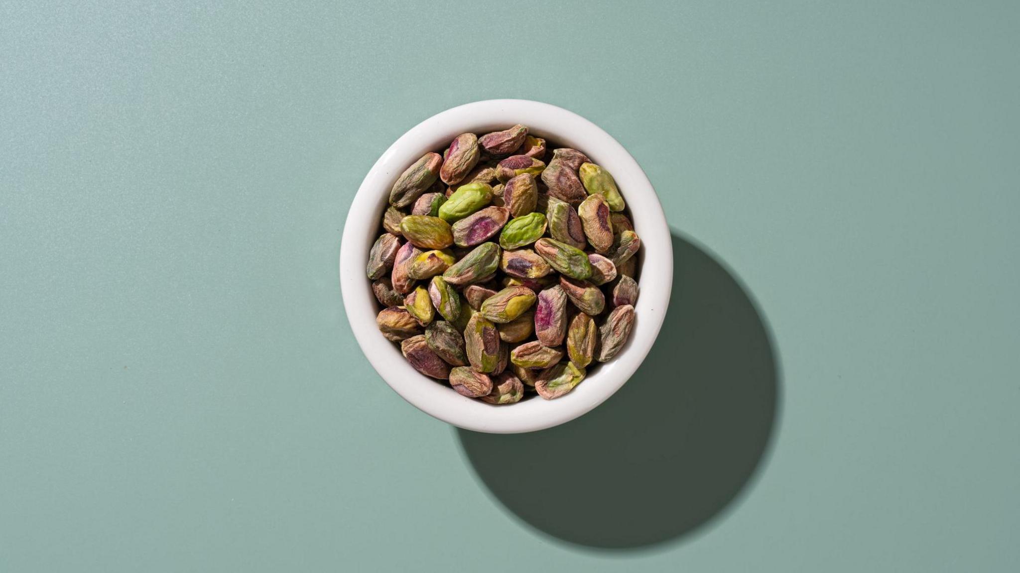 A bowl of shelled pistachios on a grey teal background