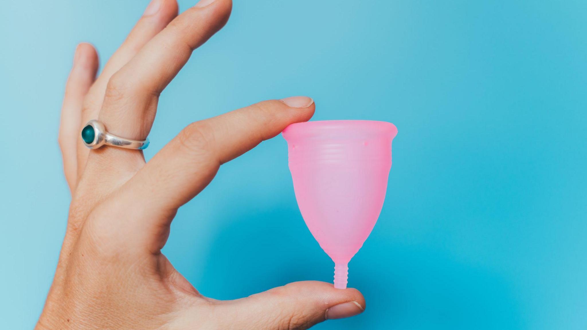 Woman holding a pink menstrual cup on blue background 