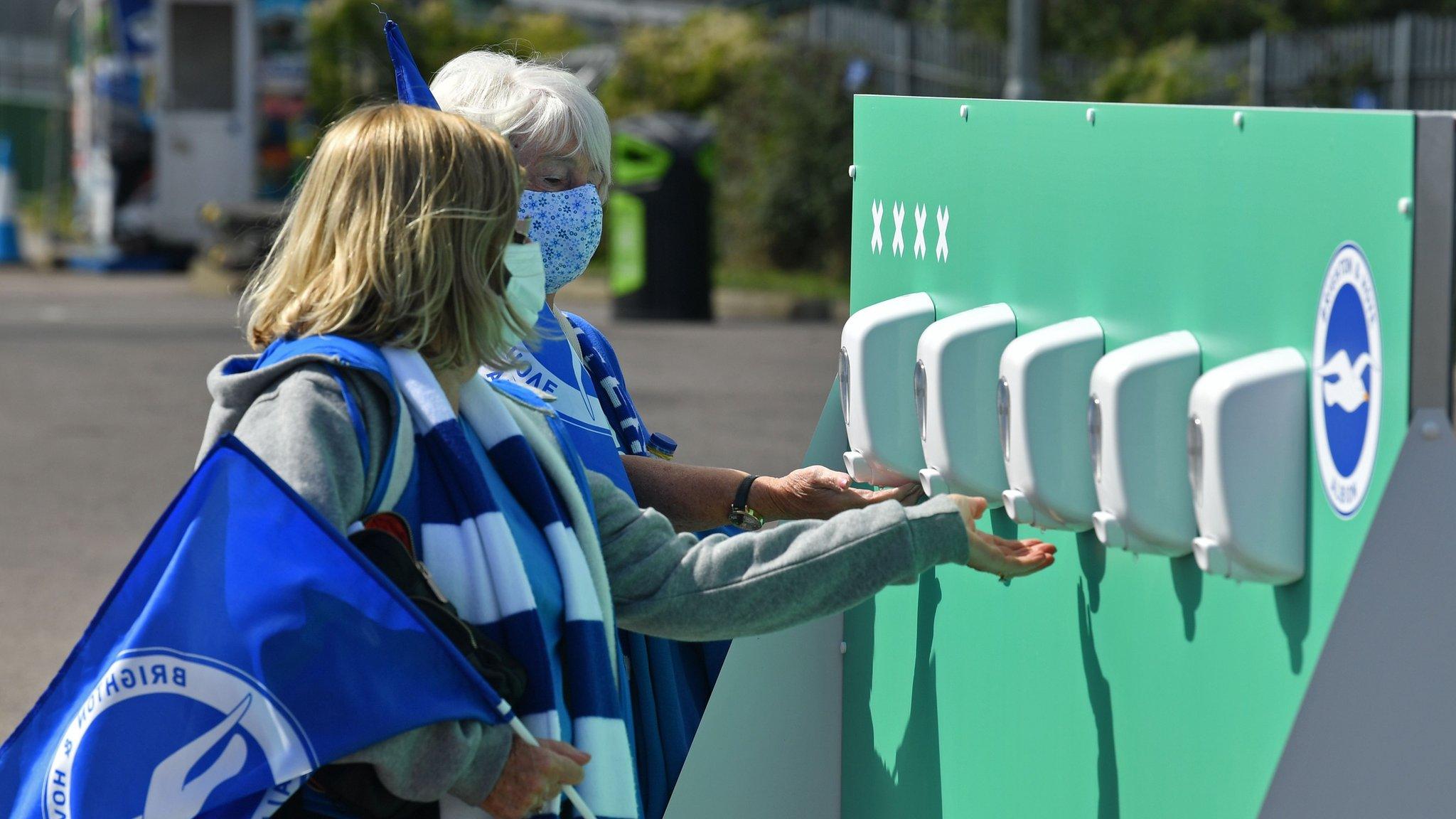 Two Brighton supporters sanitise their hands