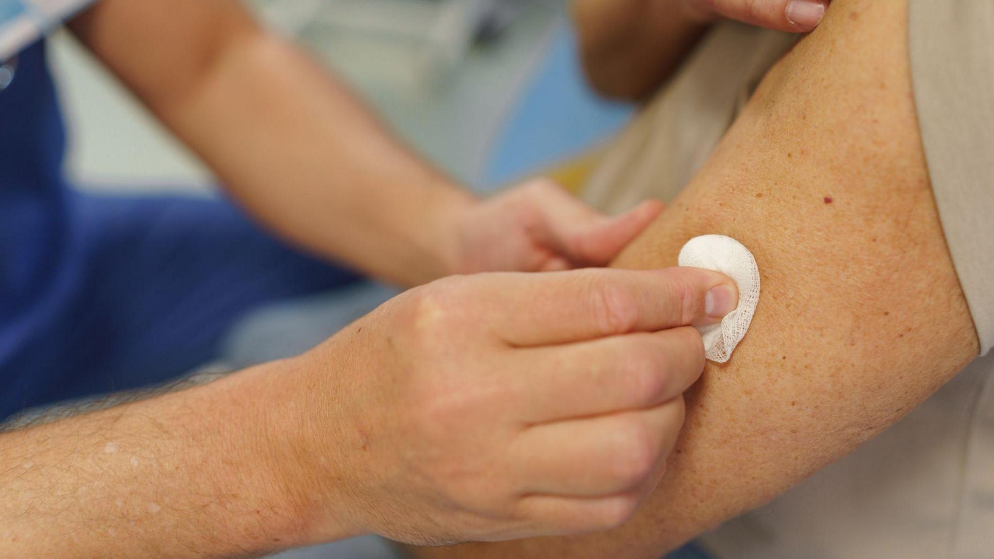A nurse pressed a cotton swab against the arm of an older patient after they have received a vaccine. 