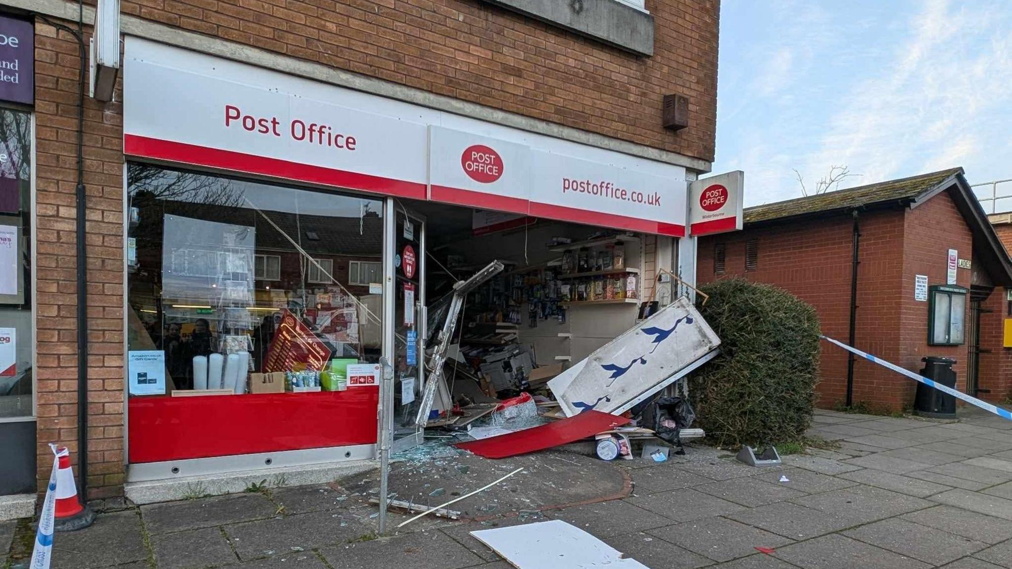 The Post Office in Winterbourne. One of the glass panels has been smashed and debris is all over the pavement. There is blue and white police tape around the building.