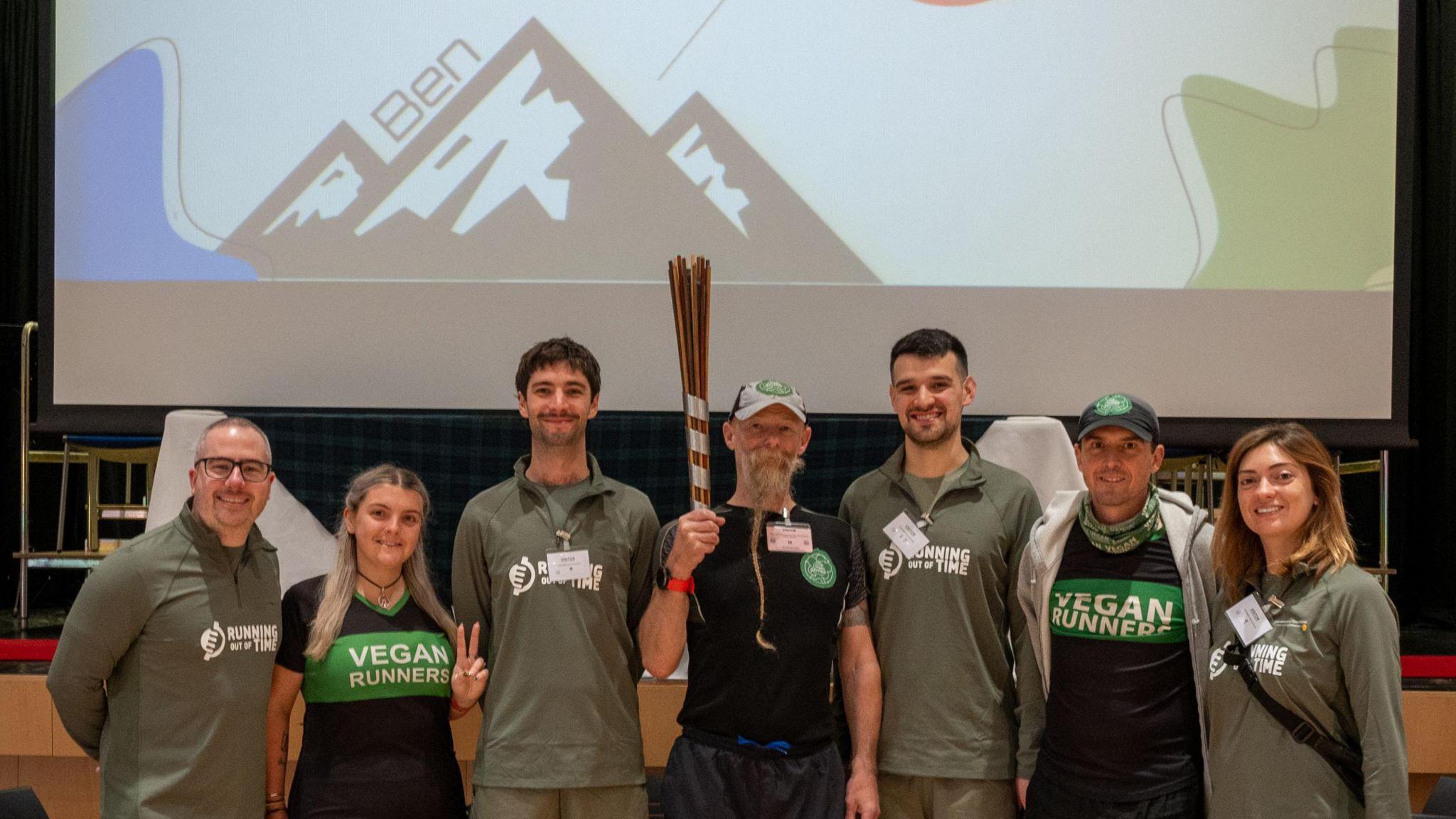 People stood in a line with one holding a relay baton made of wooden sticks