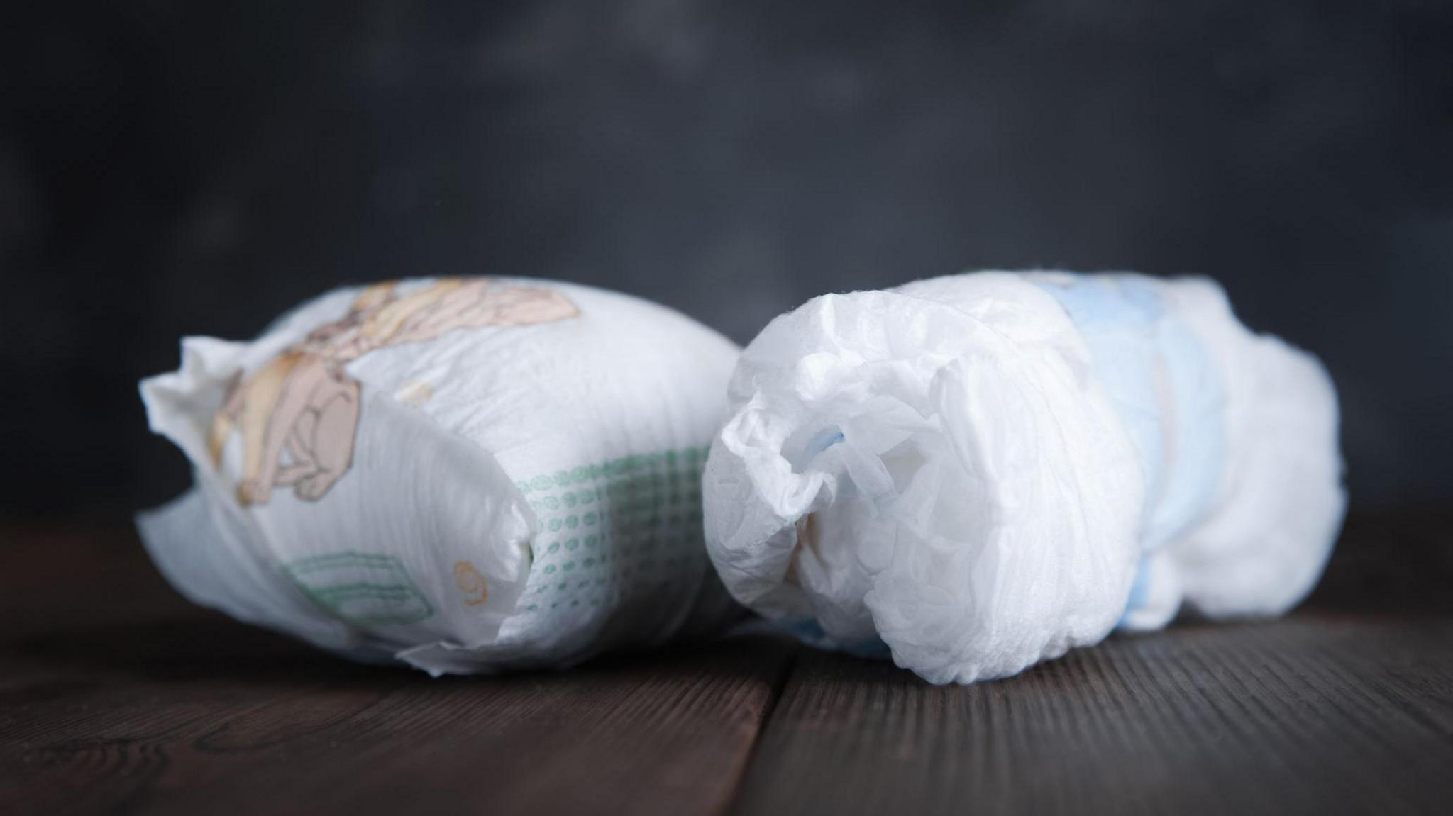 Two used nappies against a grey backdrop.