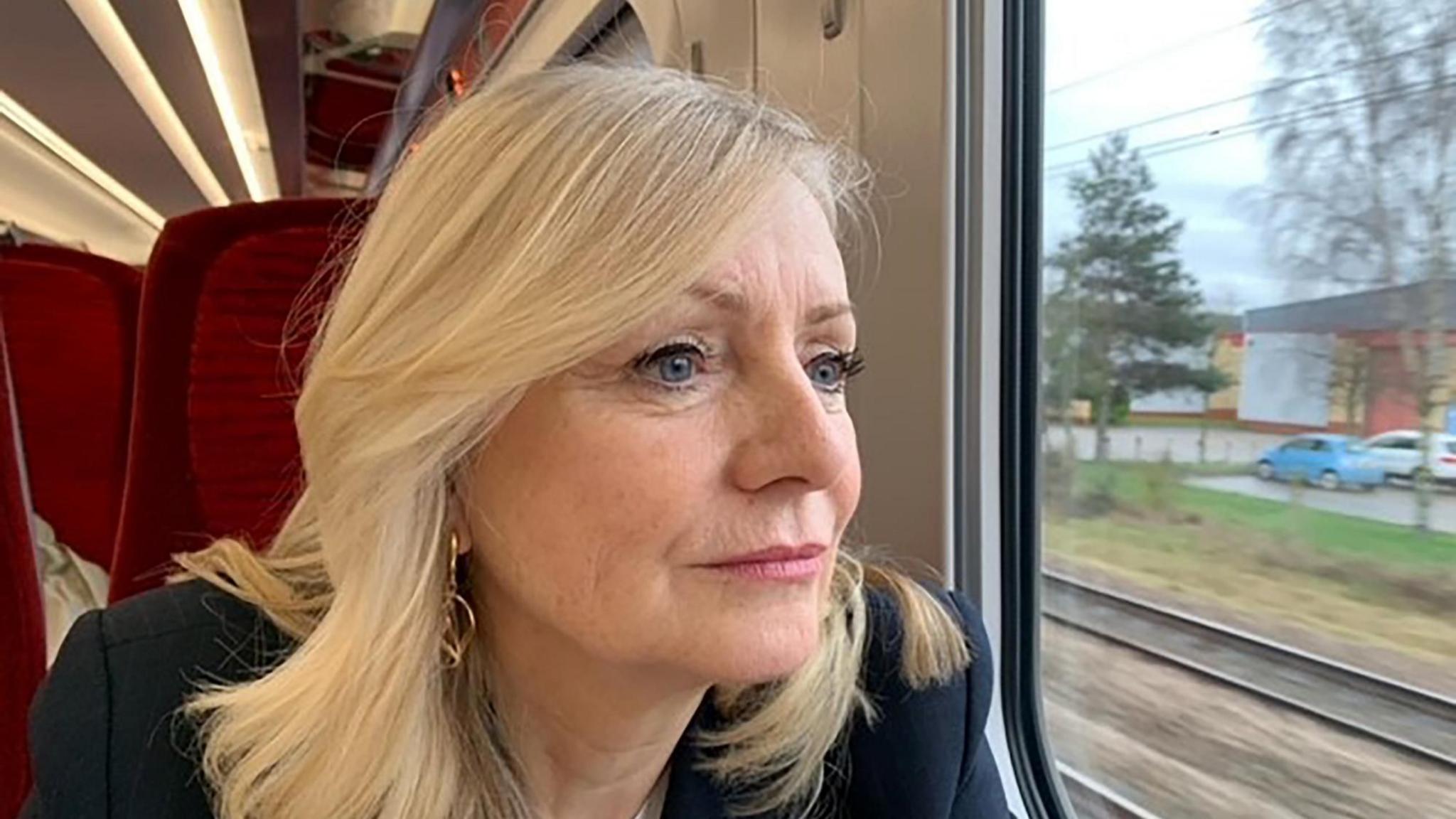 Tracy Brabin, a woman with long blonde hair, sits on a red chair on a train, looking out of the window.