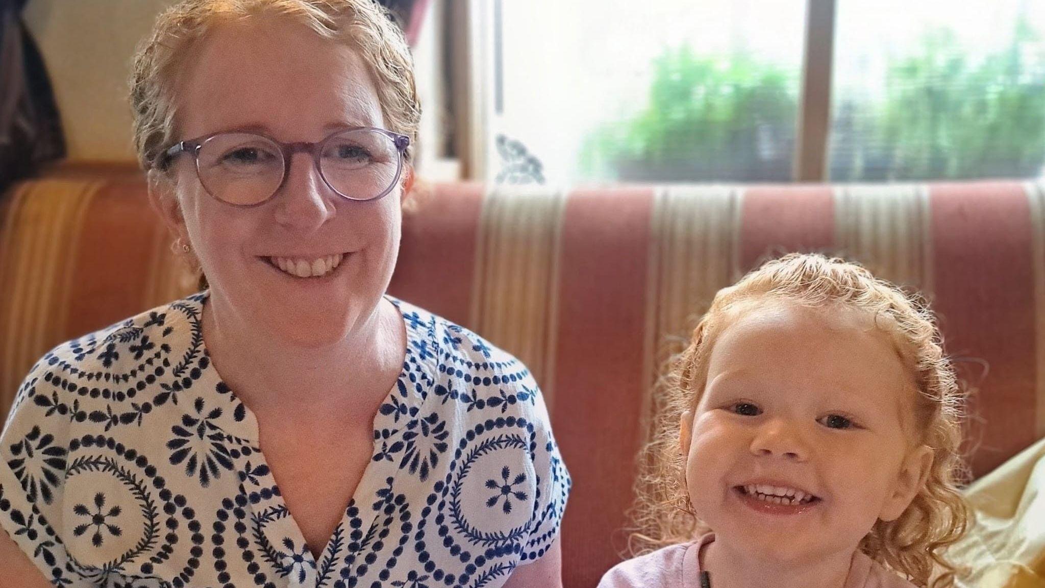 Joanne McShane and her daughter Niamh. Joanne has curly light red hair tied back, wearing glasses and a blue and white top. Niamh has light red hair partly tied back, wearing a pink jumper.