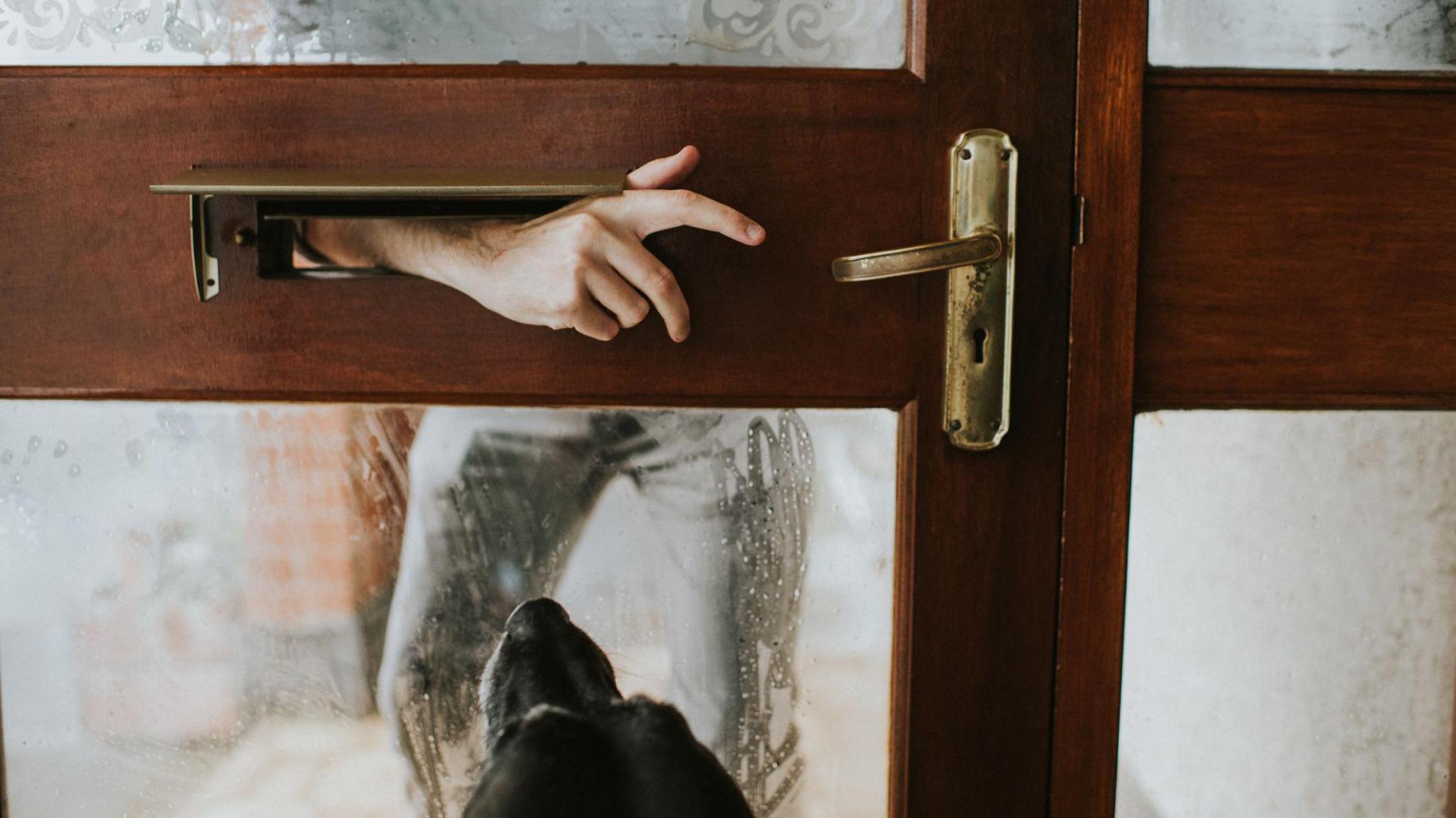 A man reaches an arm through a letterbox towards a door handle