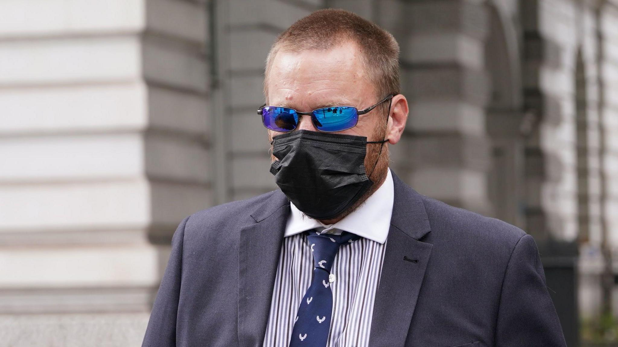 PC Craig Carter wearing a suit, tie, face mask and sunglasses