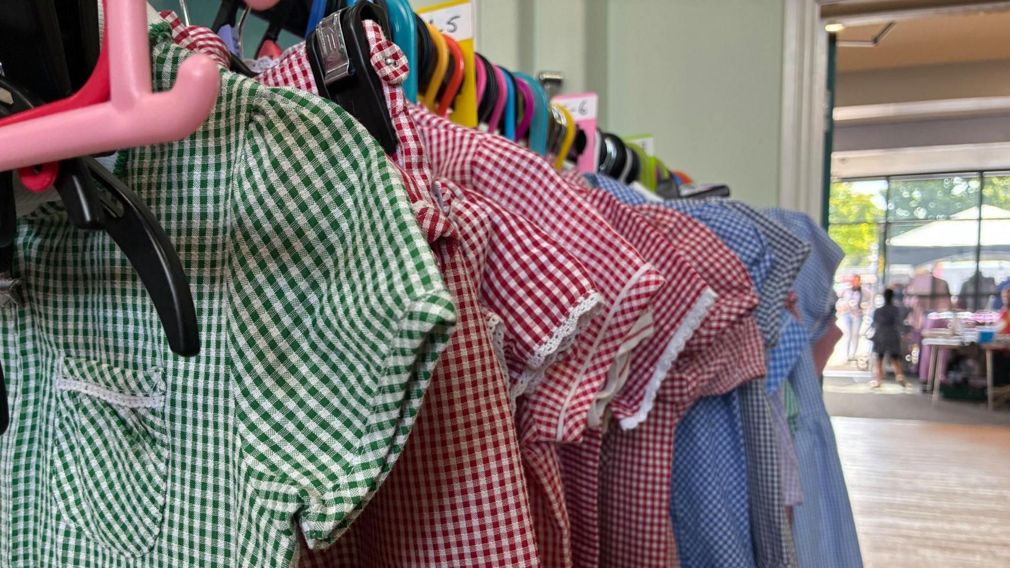 A rail of school summer dresses with gingham patterns in green, red and blue.
