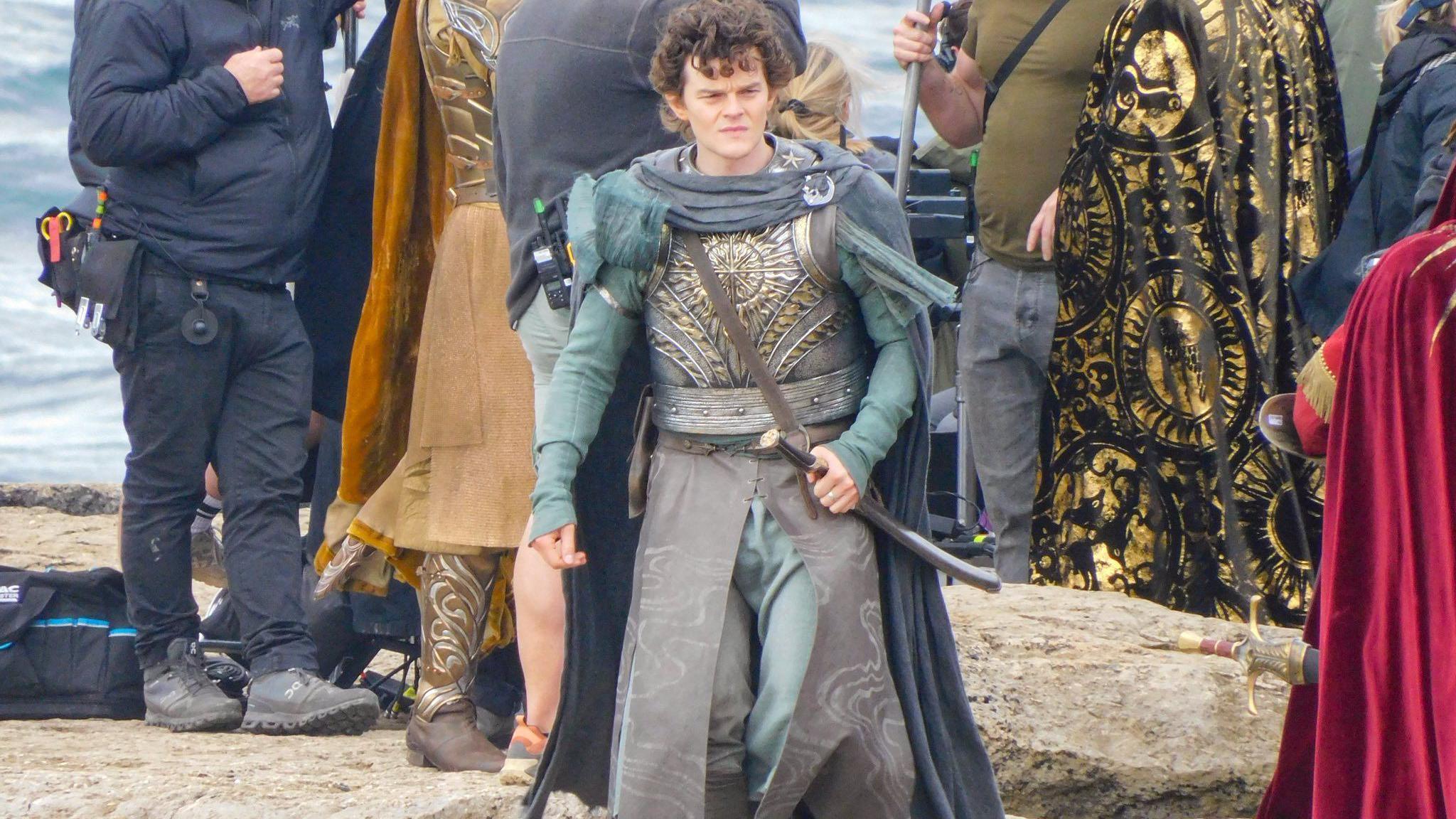 Robert Aramayo in the role of Elrond at the shooting day at Pulpit Rock. He is holding onto a sword. Other actors and filming crews could be seen behind him.