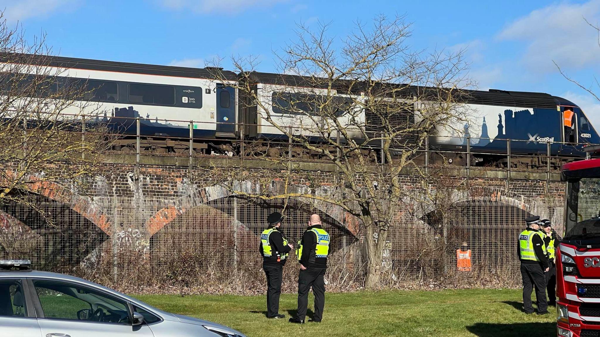 Four police officers survey the scene at the railway bridge, standing in front of the railway bridge above them