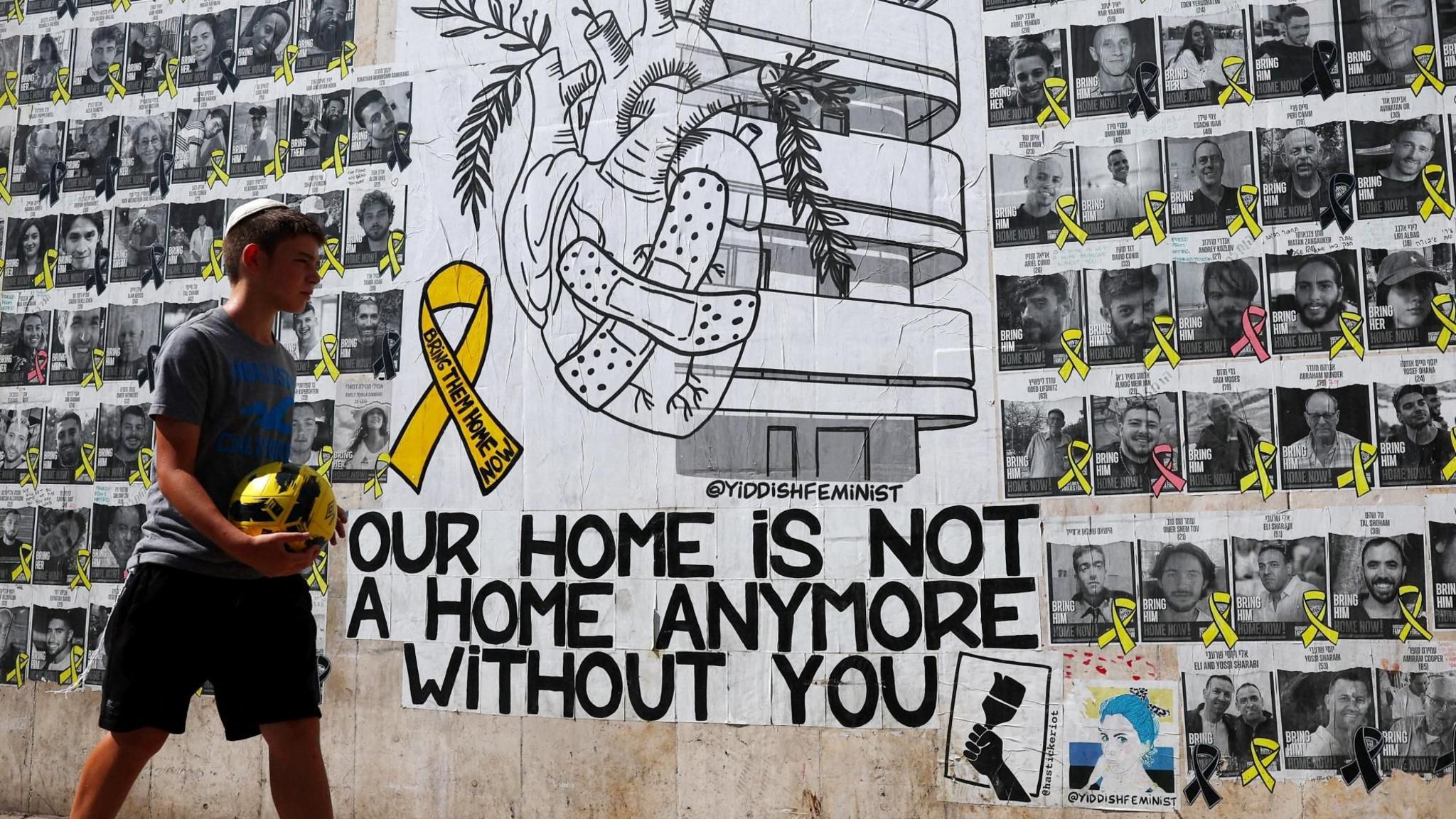 An Israeli boy walks past a mural in Tel Aviv calling for the return of Israeli hostages held in Gaza, next to posters of the hostages (15 August 2024)