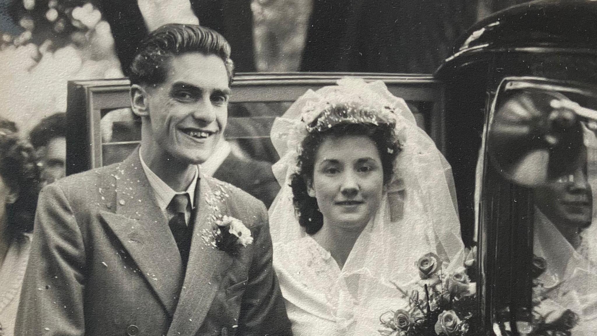 A black and white photograph shows the couple on their wedding day with confetti all over them while they get into a black car. 