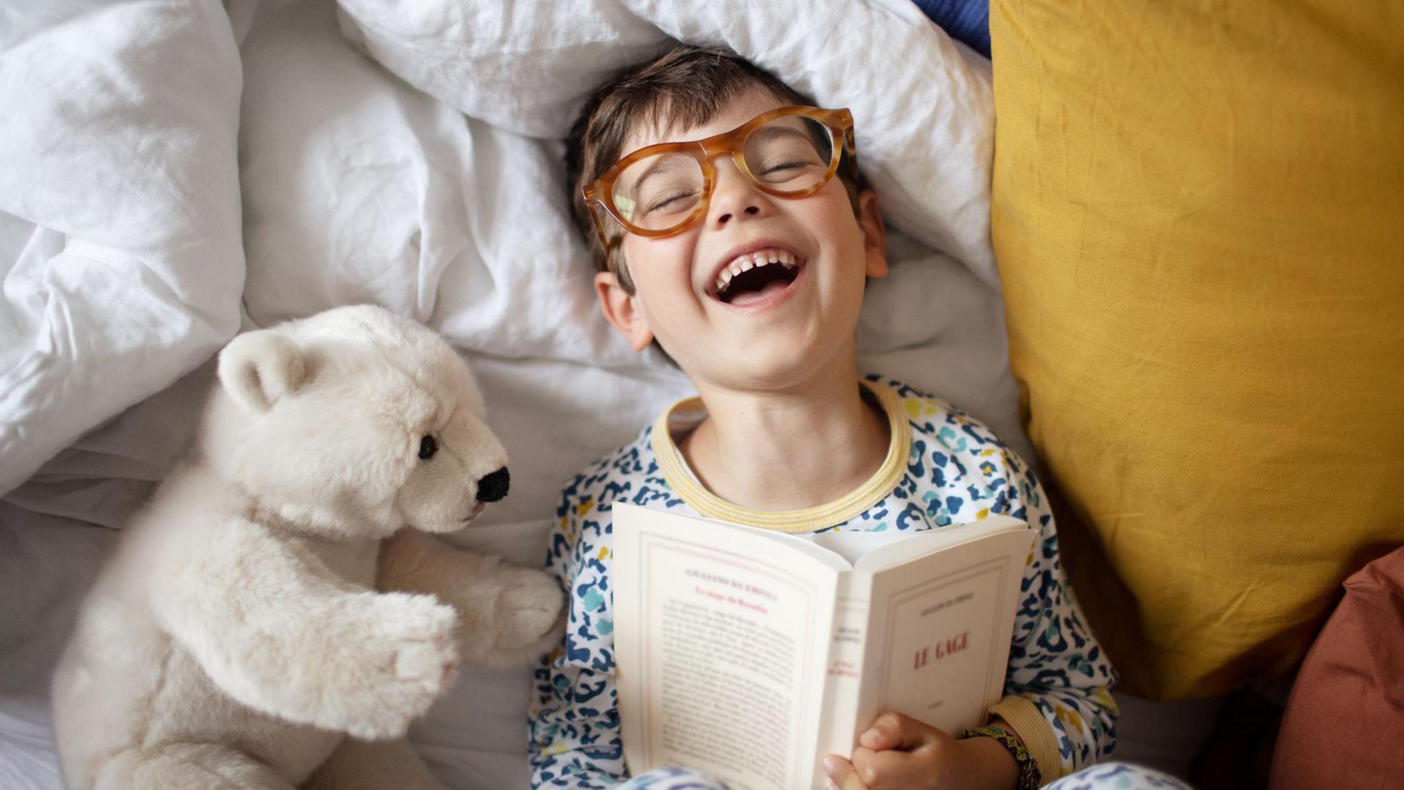 a little boy in bed reading and laughing