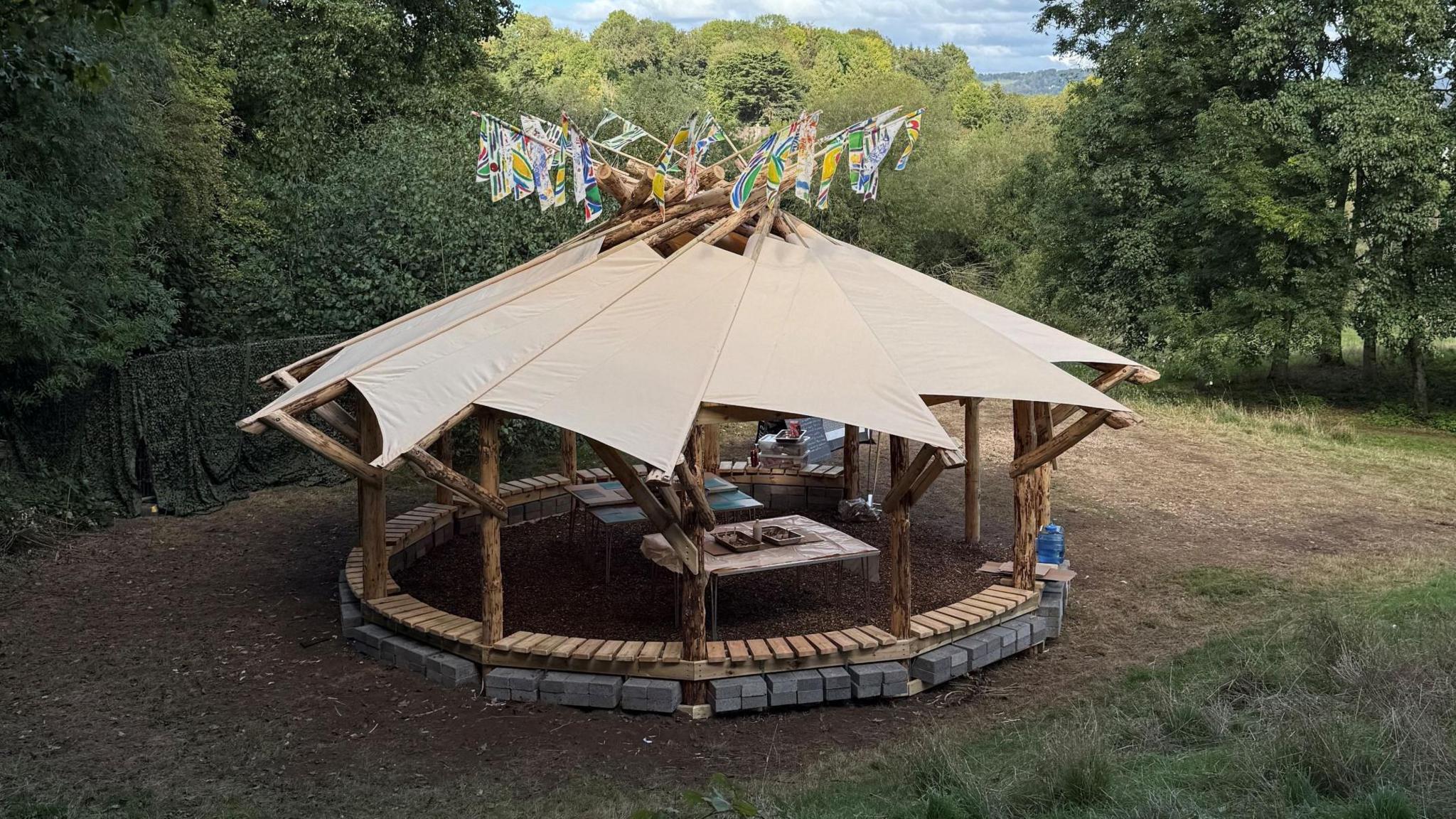 An outdoor classroom covered by a canvas roof, with multicoloured triangular flags strung across, set up for group learning.