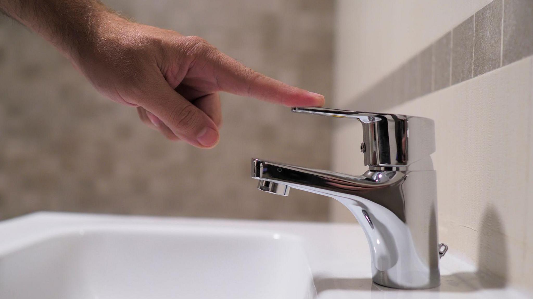 Hand pressing down on water tap at sink