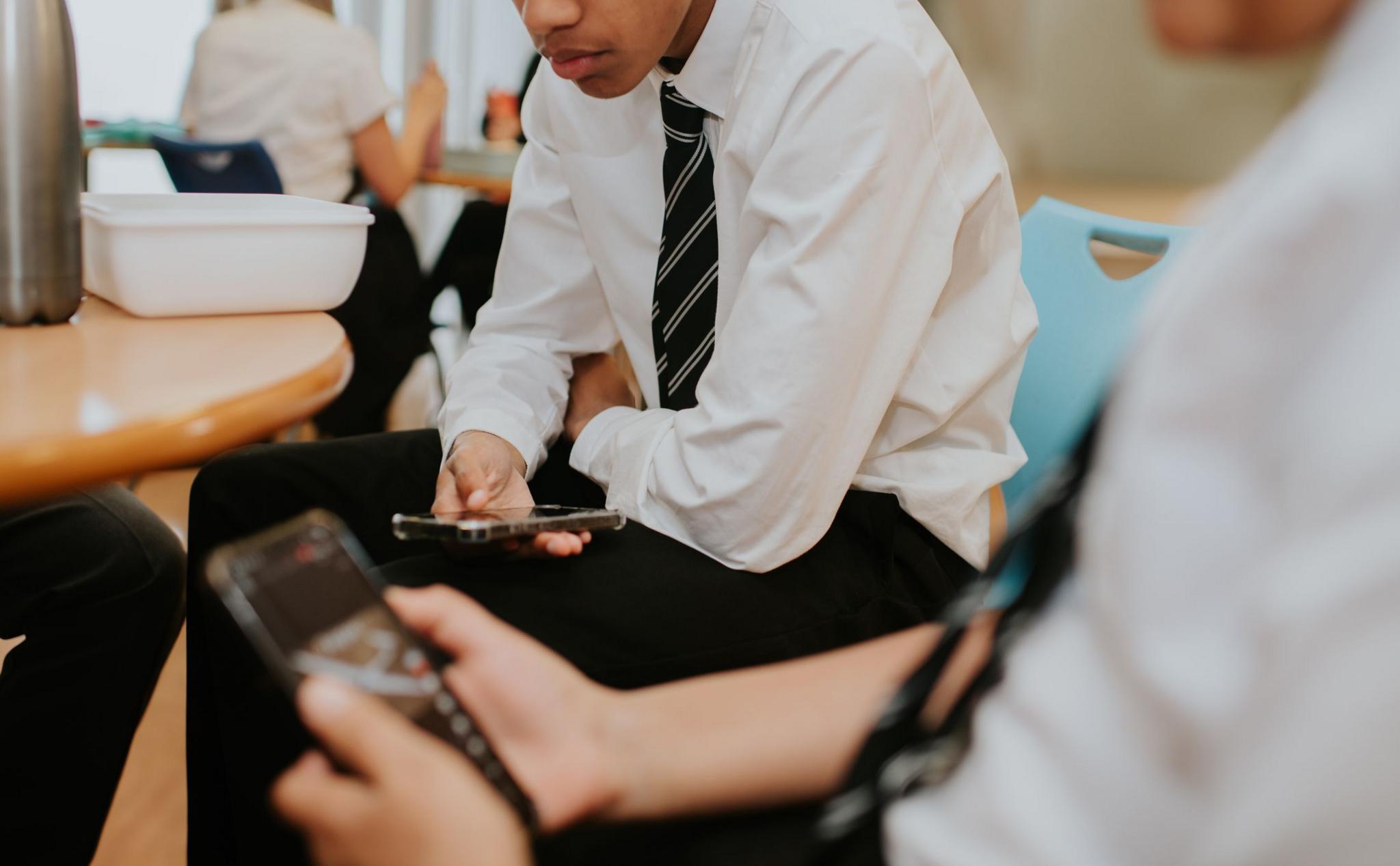 Two school boys stare at their smart phones during the school lunch break in a cafeteria.