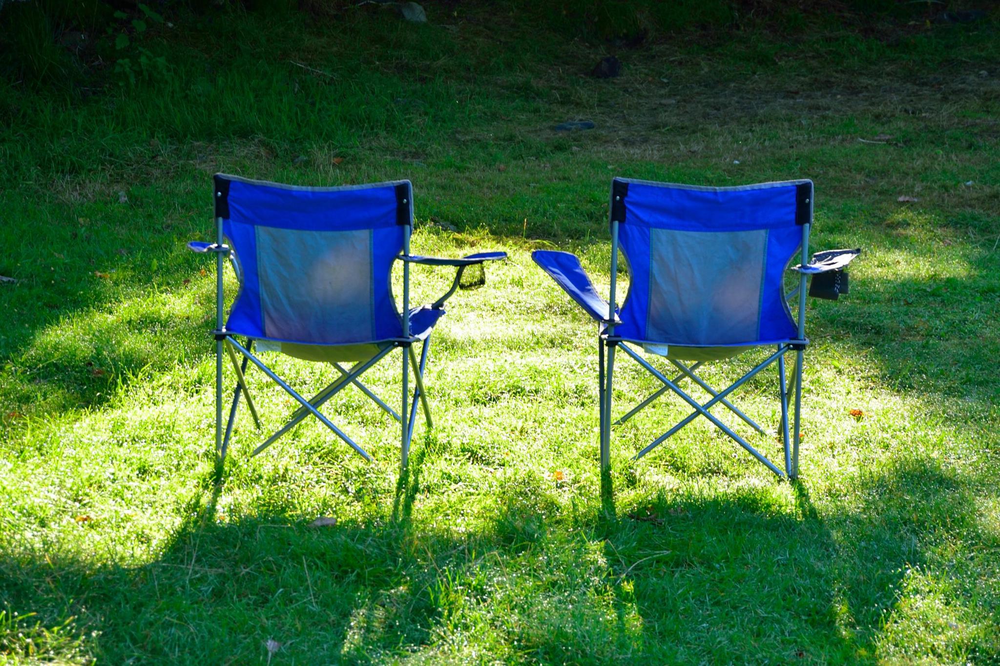 Two blue camping chairs pictured from the back on grass