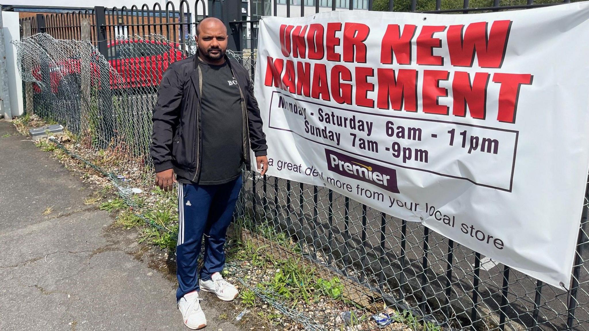 Thinesh Rajavatnam next to his banner that states 'under new management'