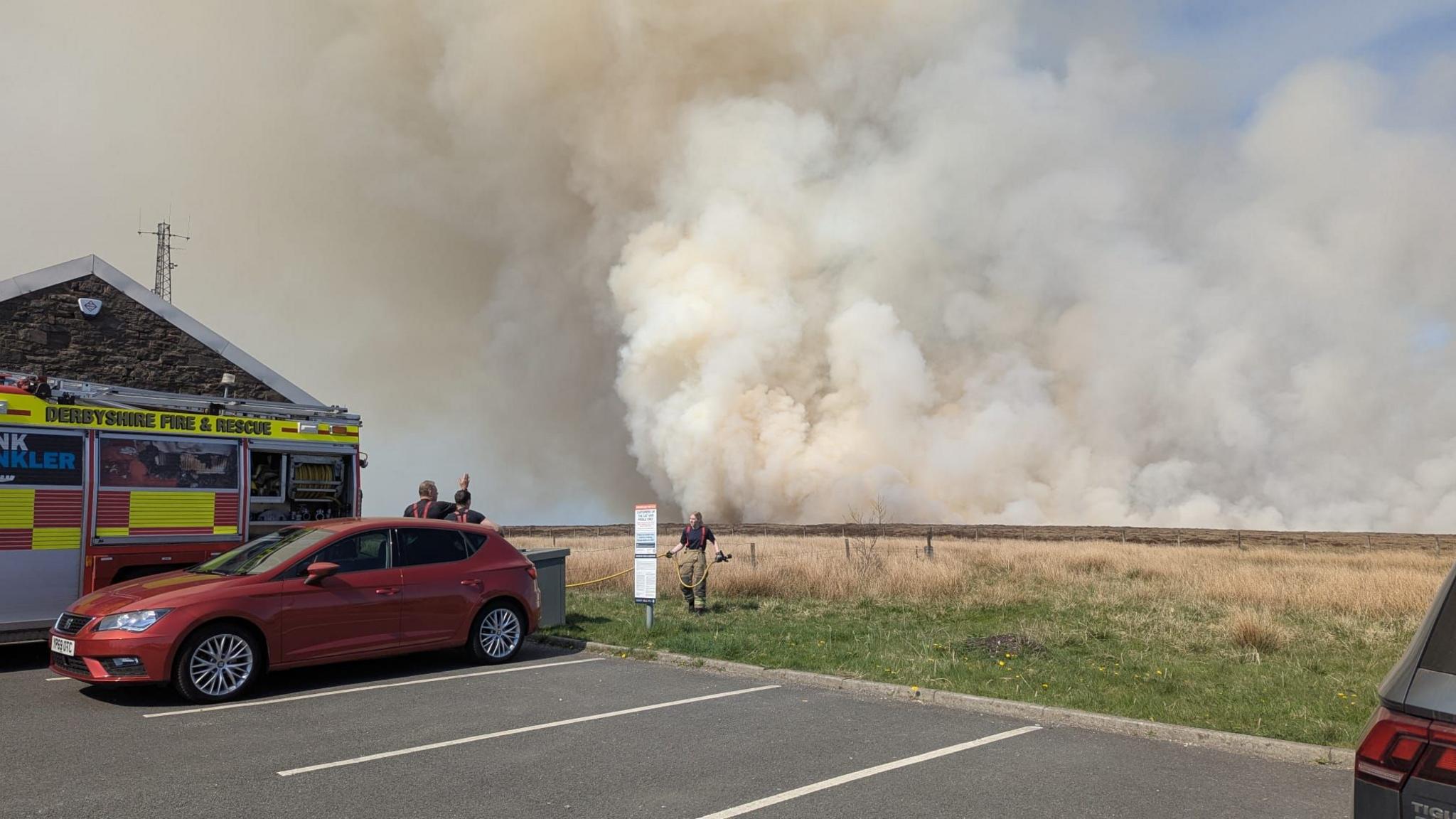 Fire crews in a car park with smoke rising over moorland in the background