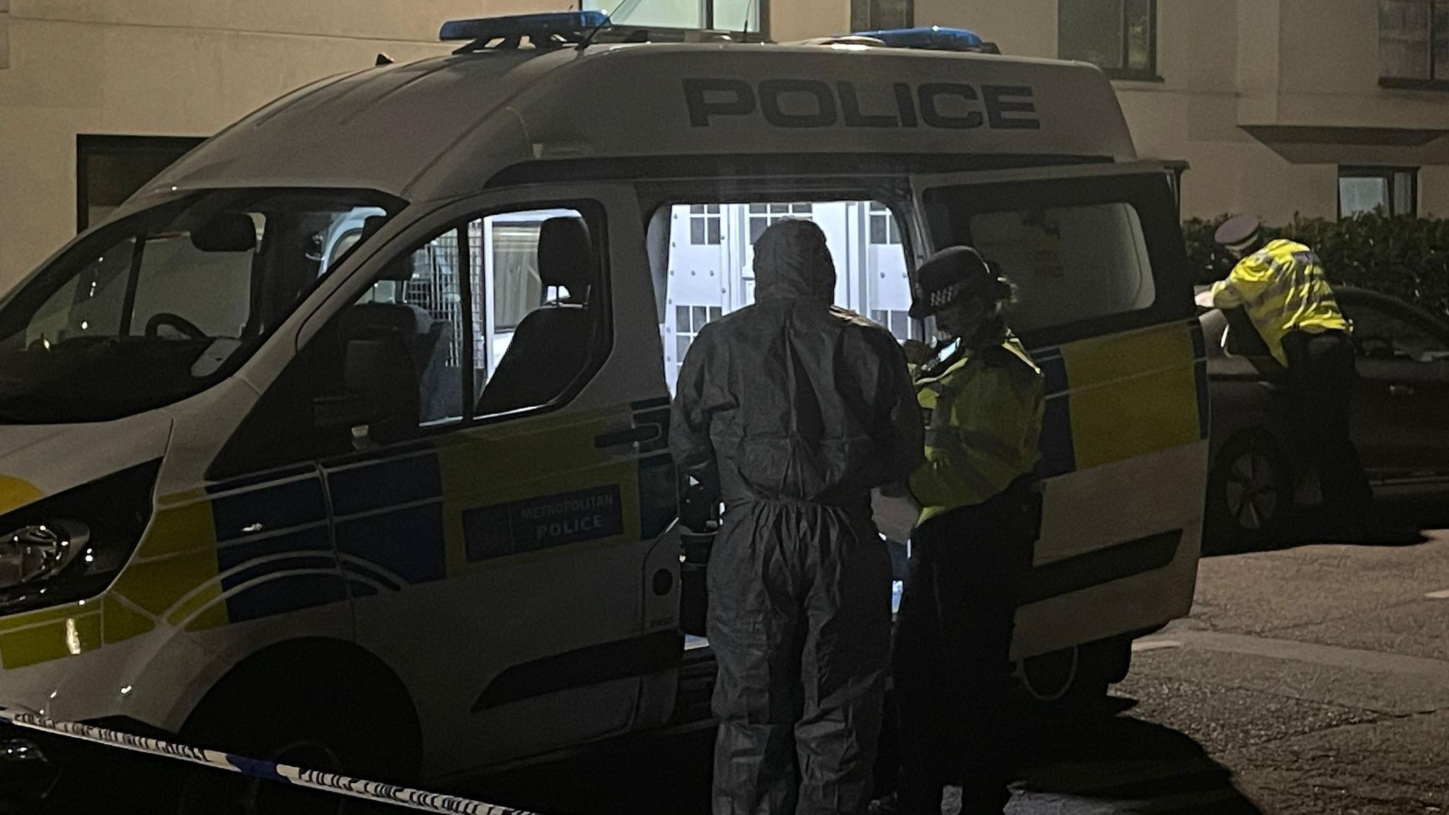 A forensic officer and a police officer stand by a police van