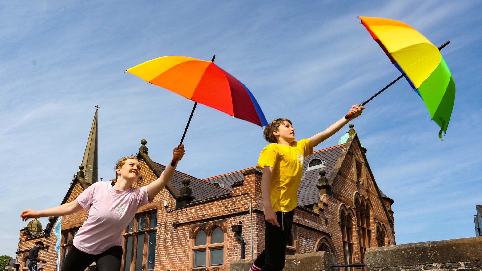 In your space performers holding colourful umbrellas