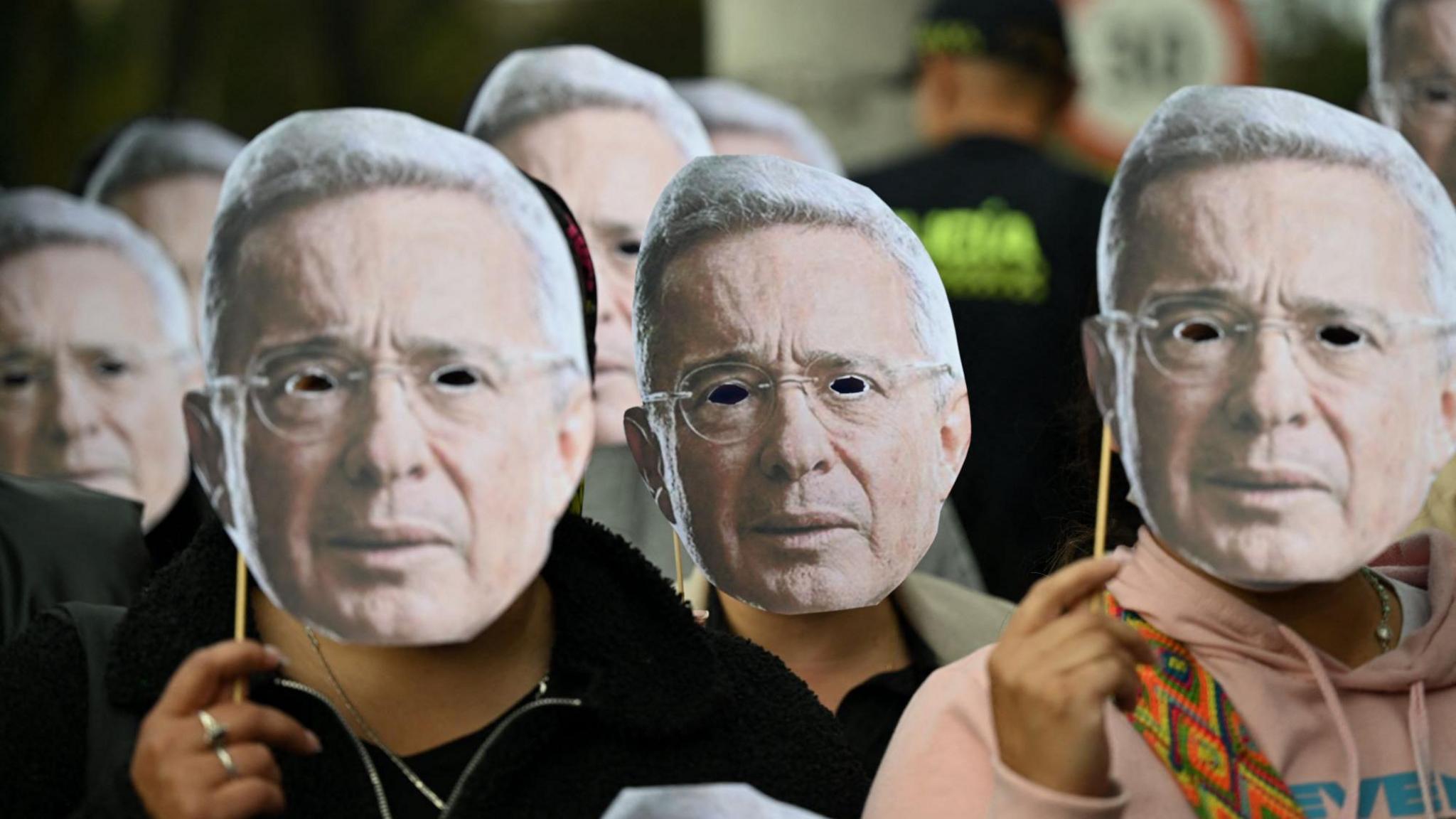 Uribe supporters wear masks of the former president with cut out holes for their eyes, outside court in Bogotá.