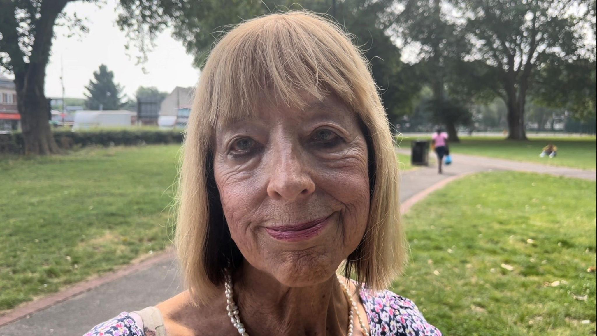 Roslyn Byfield  standing in a park with trees behind her