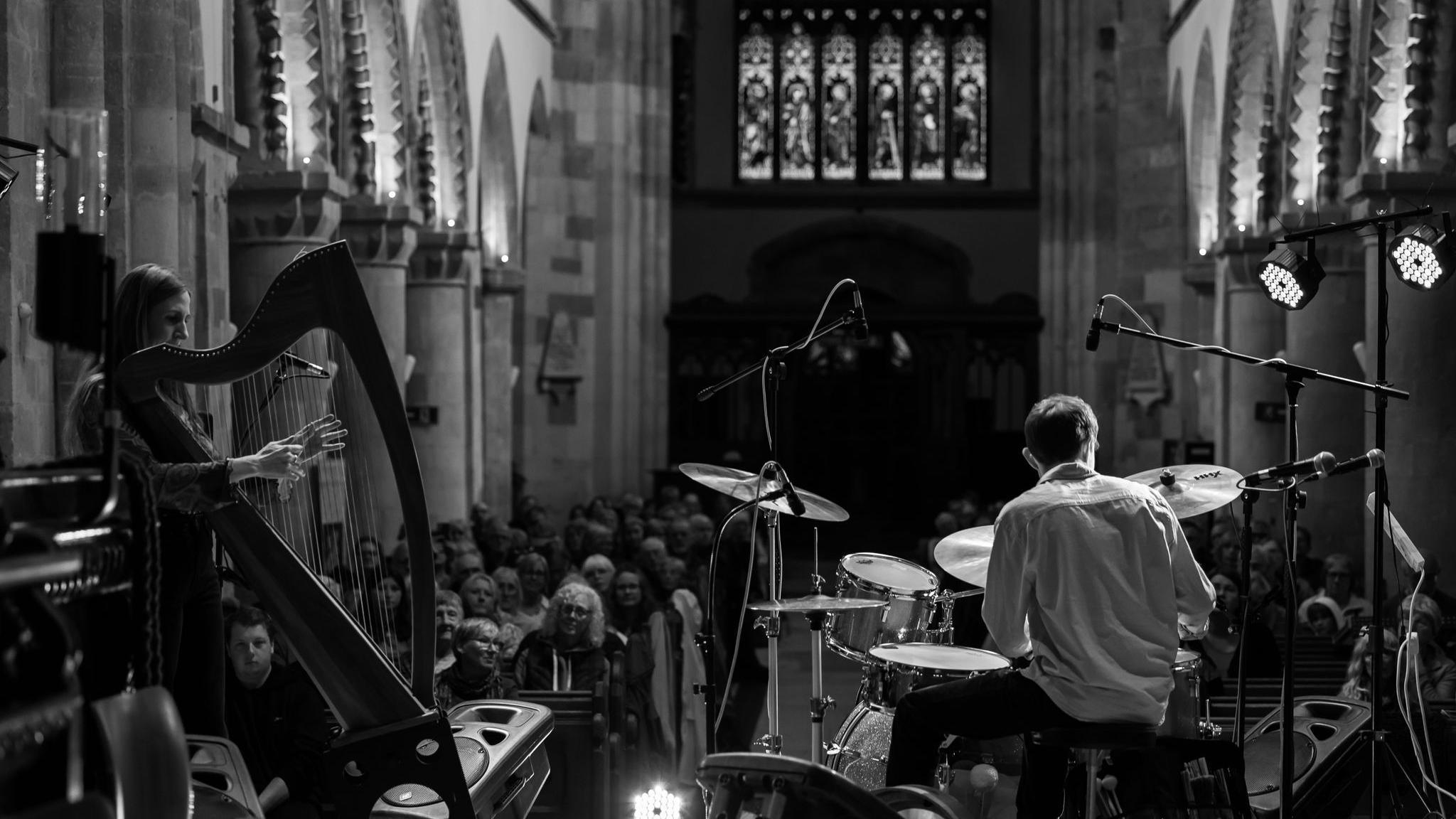 A woman on a harp and a man on some drums sat at the front of a church