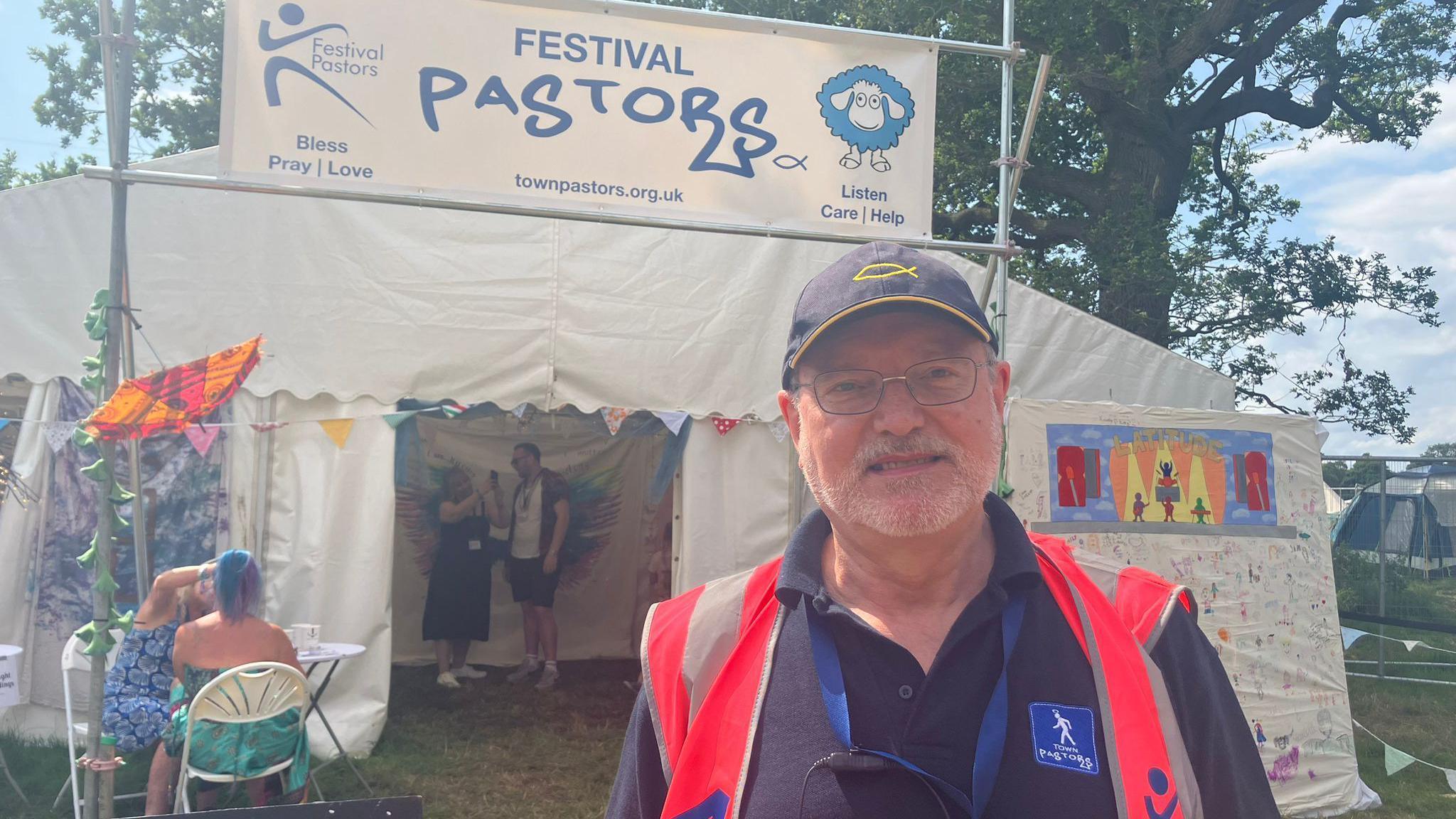 Peter Livey in a festival pastors hi-visibility vest stands in front of their welfare tent