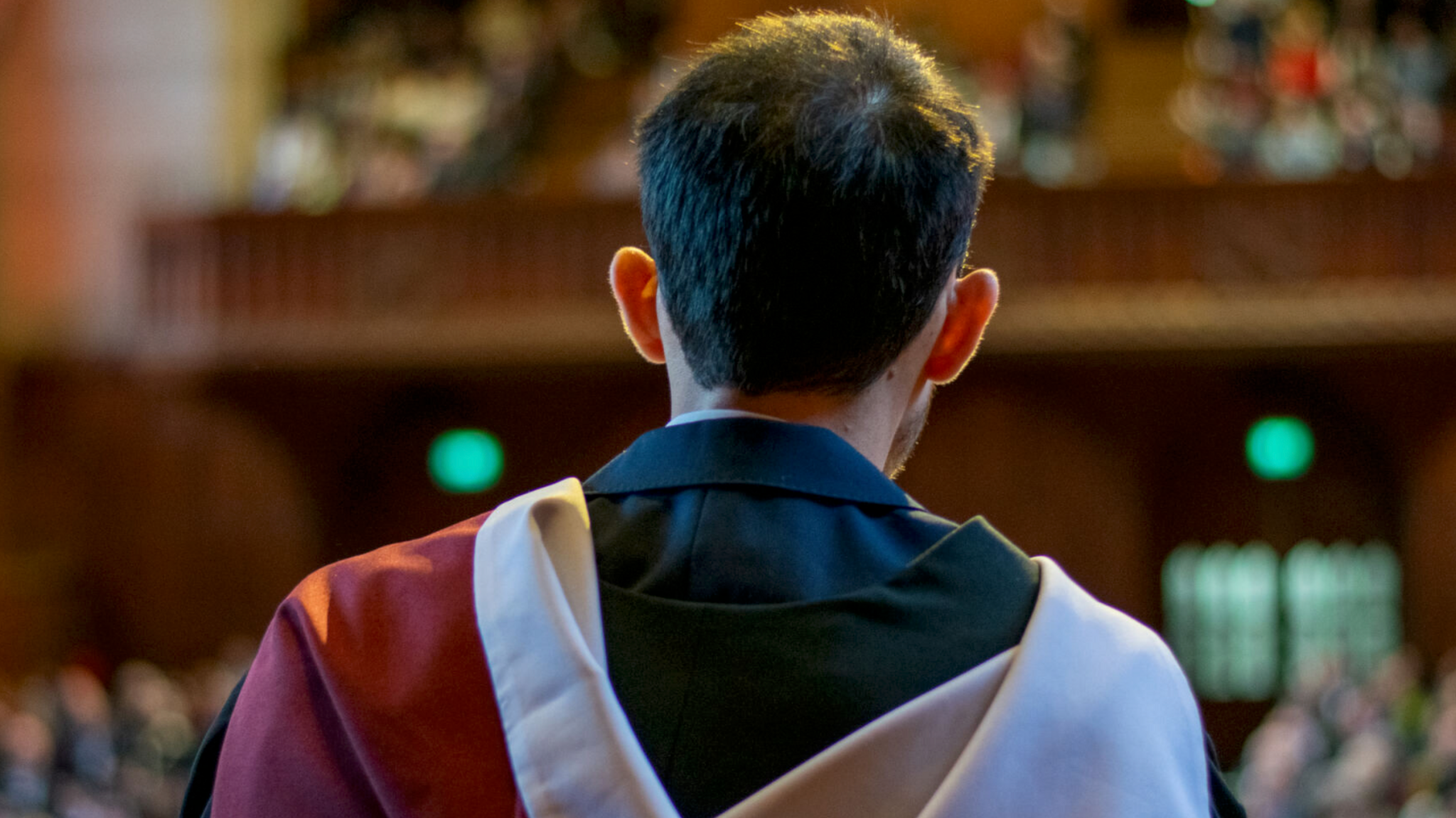 A view of Mr Fatthouh from the back. He has on a dark blue suit under his robes and is facing a crowd of more than 1,000 other graduates and their loved ones.