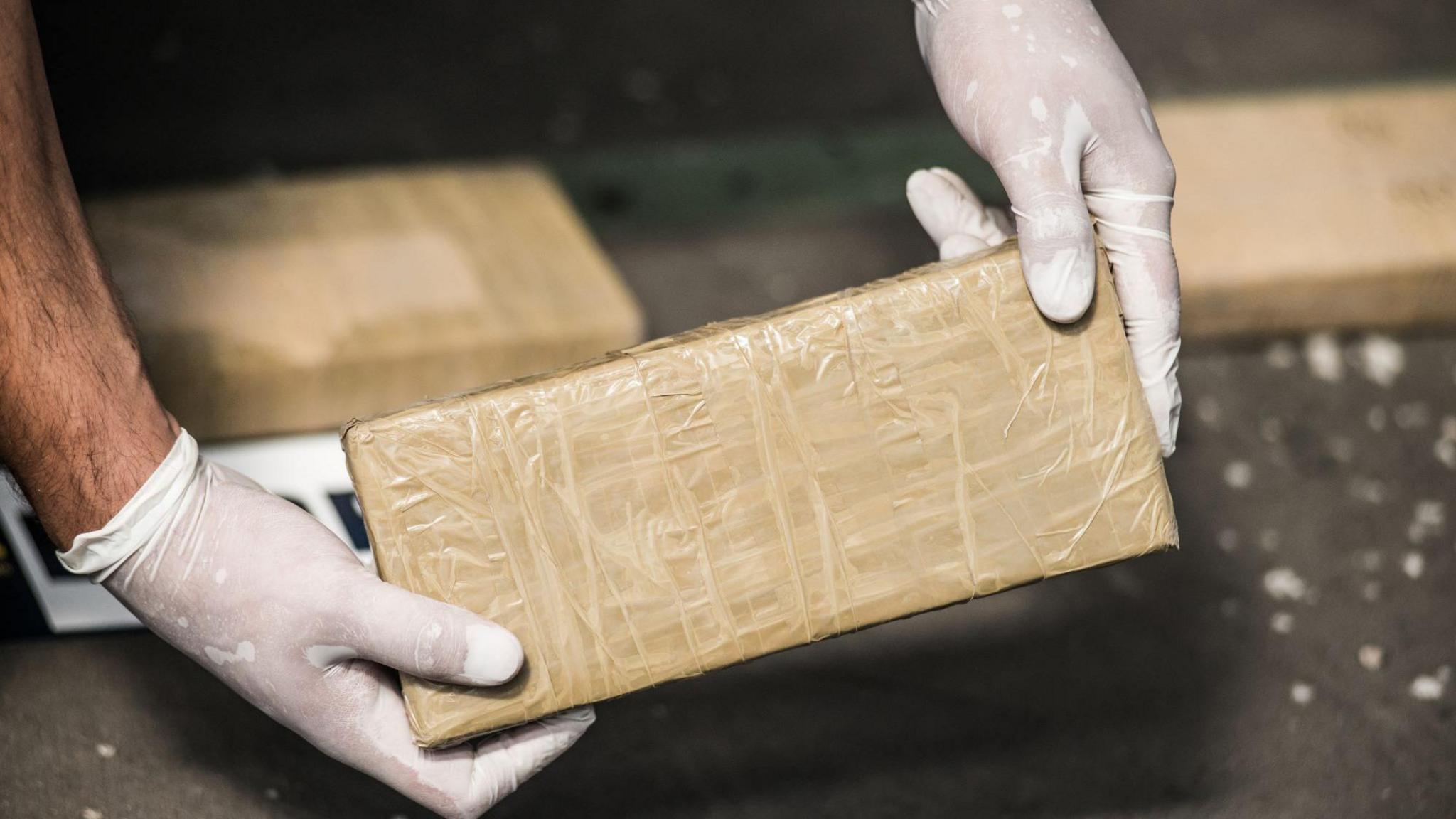 Generic image of hands wearing white gloves, holding a wrapped up cardboard box 