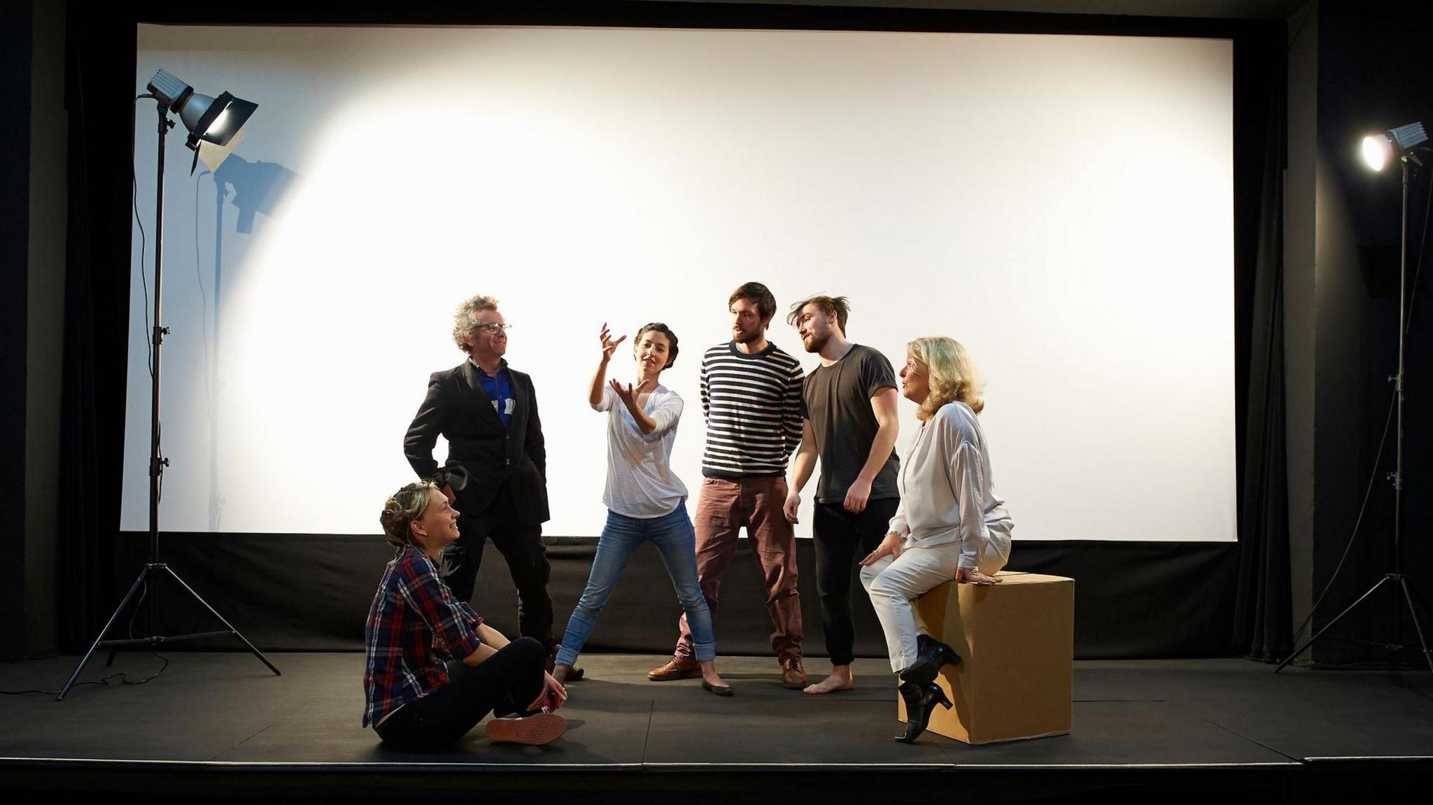 a group of six performers act out a scene on a state with a white background behind them