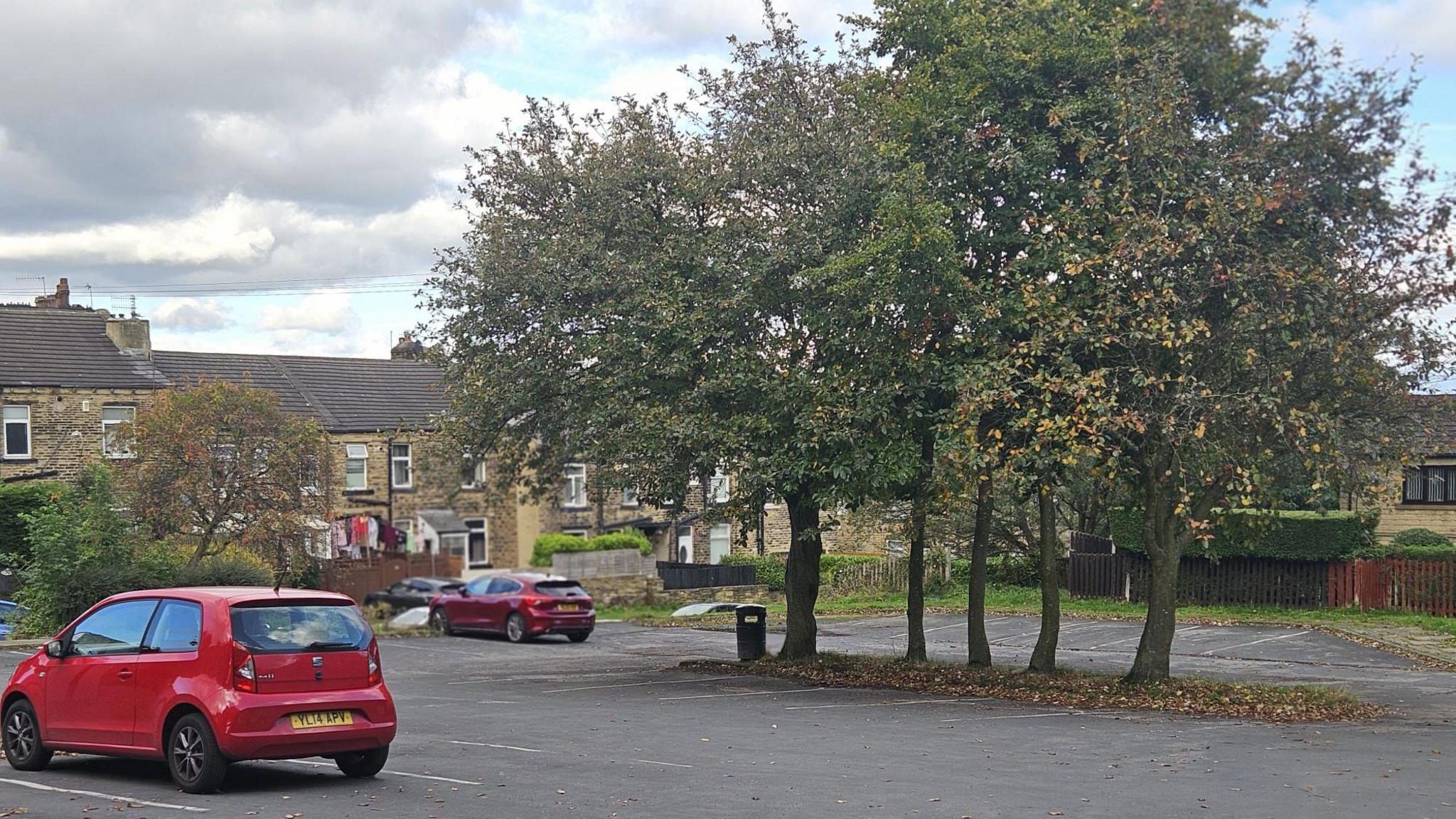 A grey-tarmacced car park with just two small red cars parked in it.