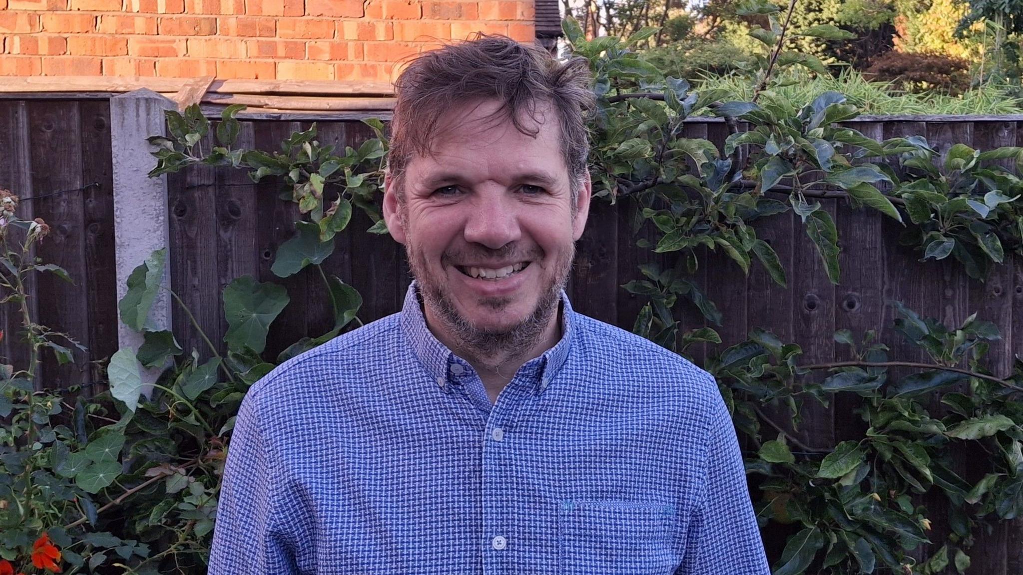 Prof Robert Dryfe smiling at the camera while standing in front of a garden fence