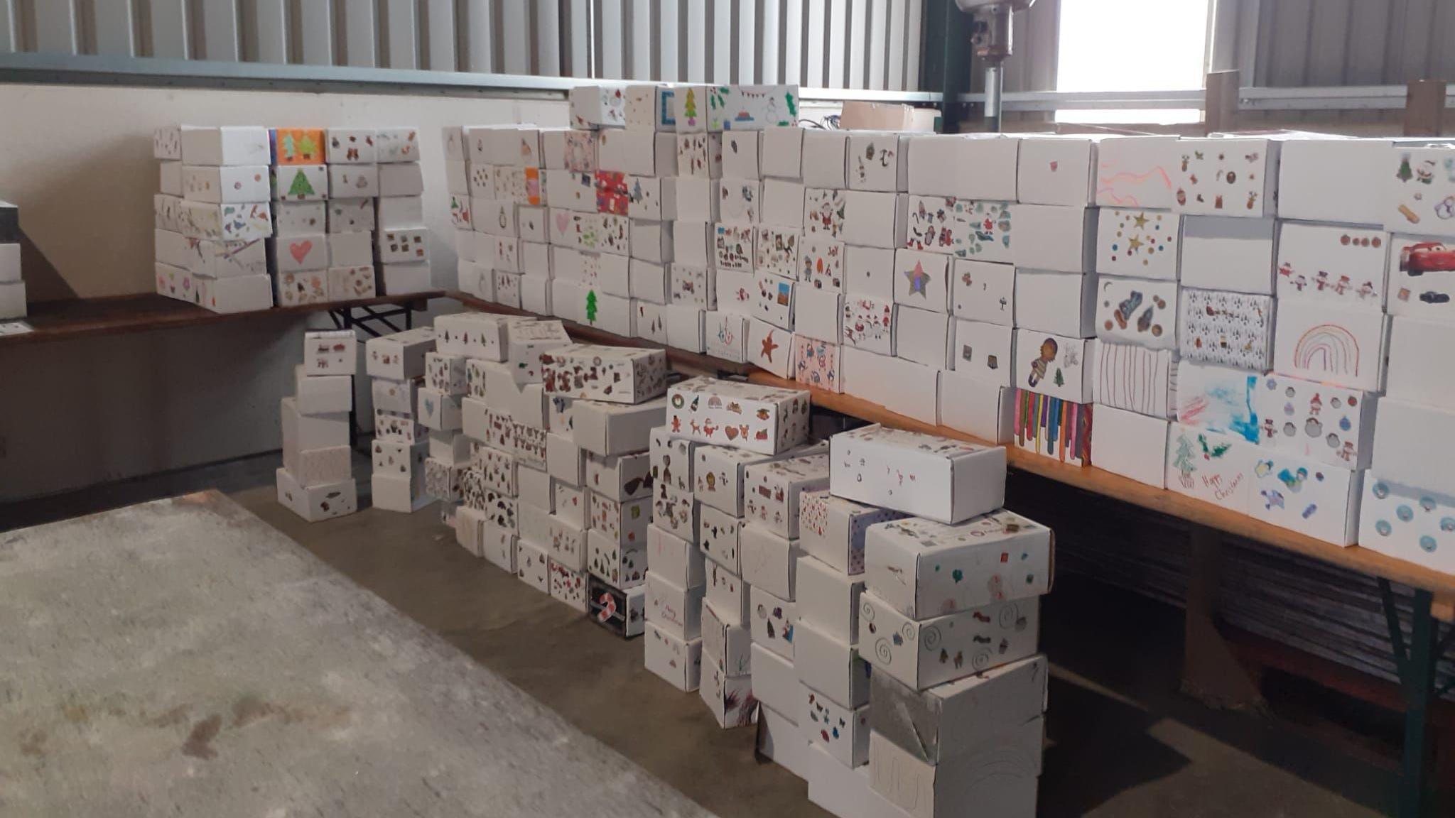 Around 100 large white shoebox are stacked up in piles in warehouse. Each shoebox has decorated with different drawings and stickers